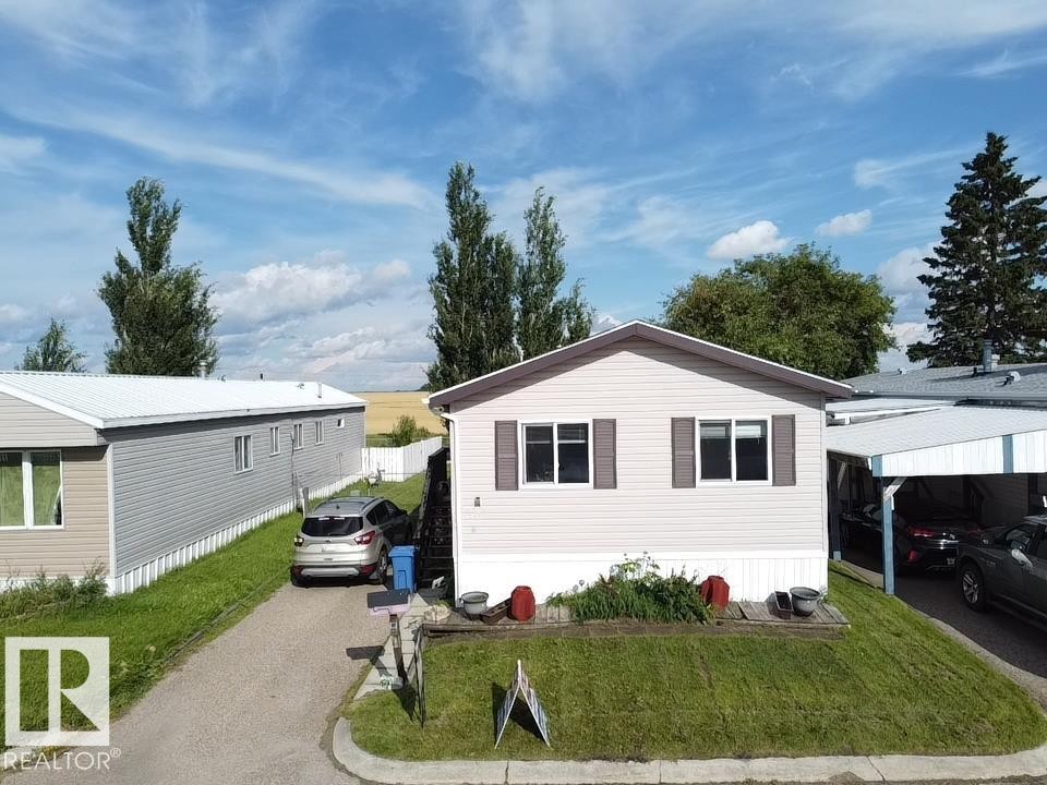 Single-story property with light-colored siding, dark window shutters, a carport, and a sloped grass lawn - #56 4202 45 St, Wetaskiwin, AB - Outdoor
