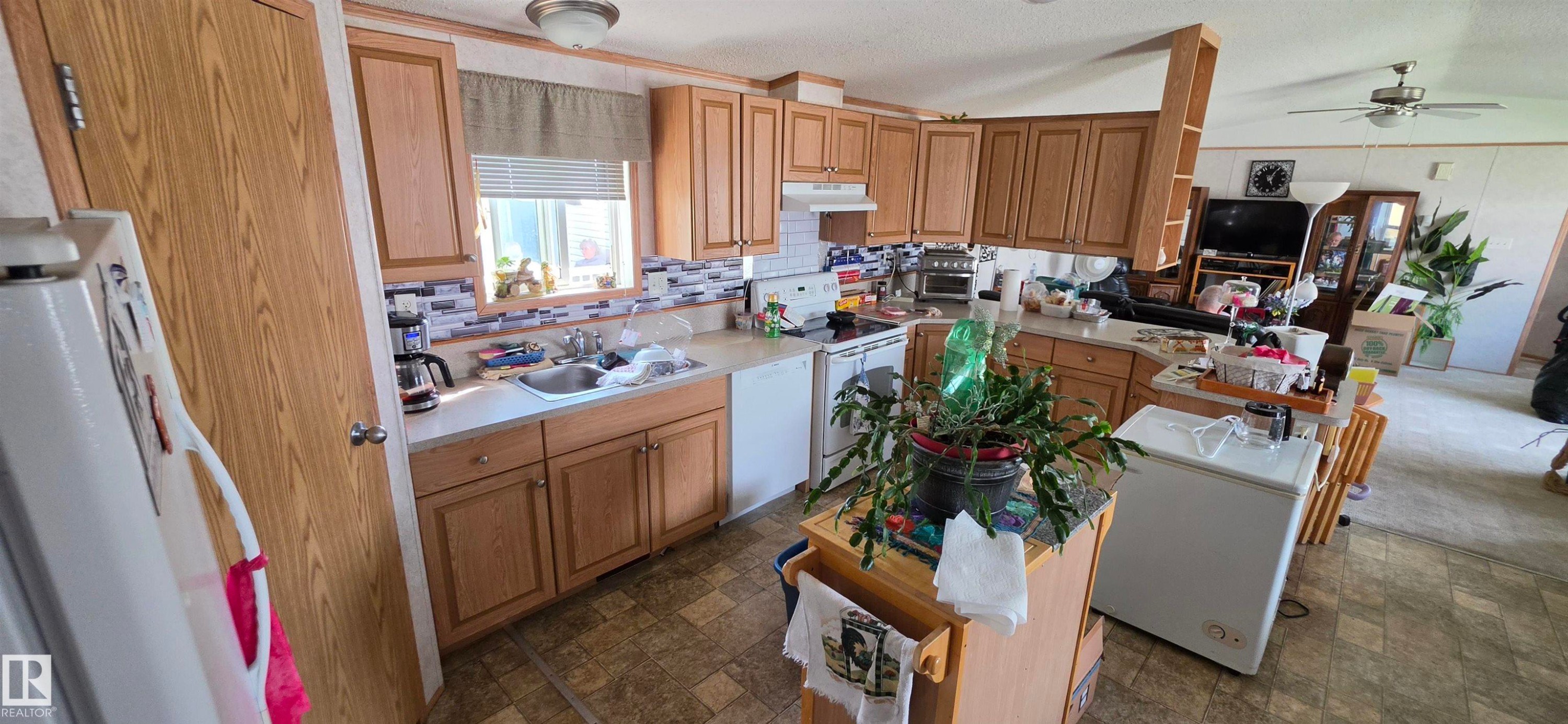 Kitchen featuring wood-finish cabinetry, light countertops, a tile backsplash, and a double basin sink - #56 4202 45 St, Wetaskiwin, AB - Indoor