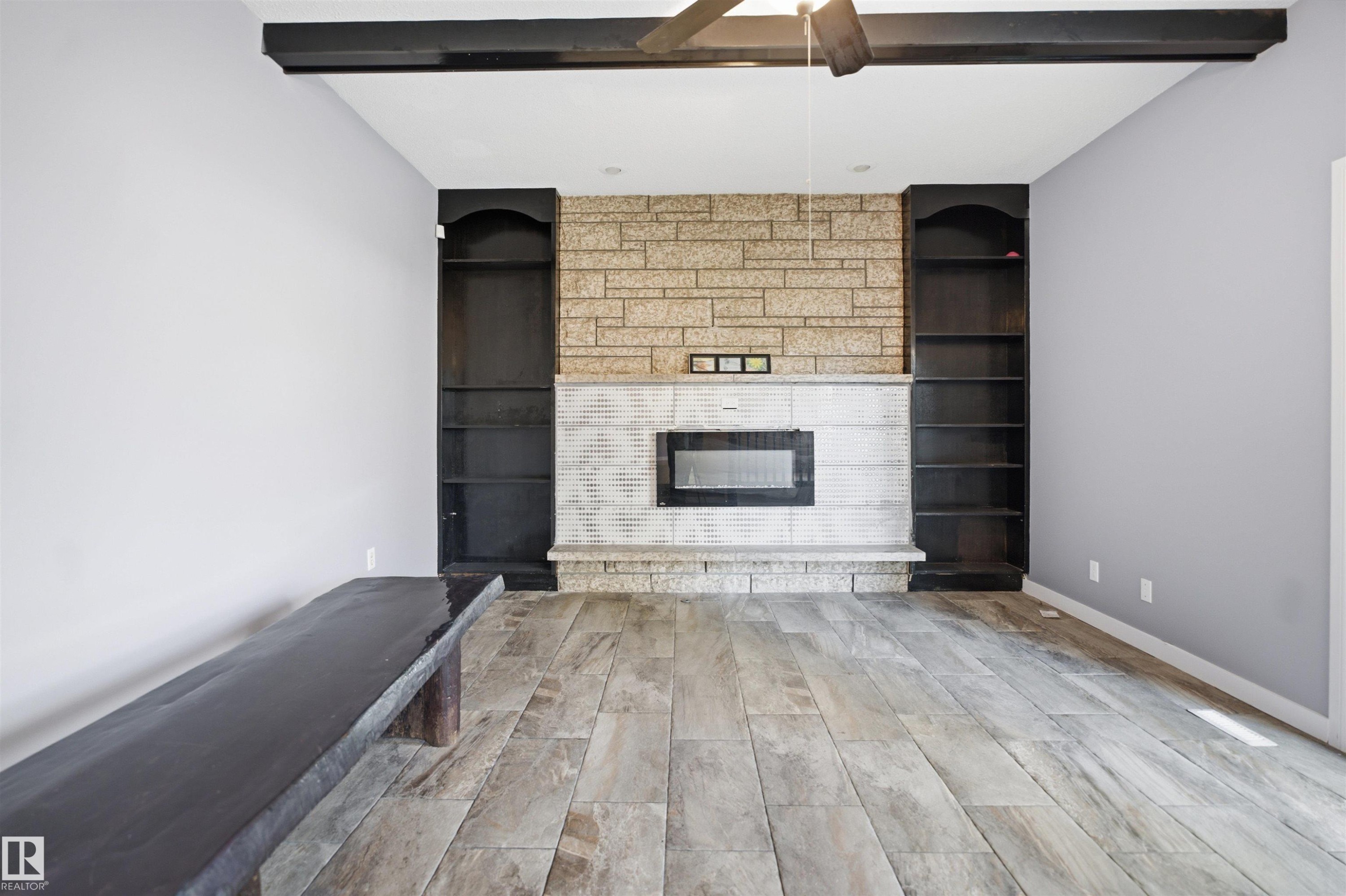 Wood-finish flooring, stone-clad fireplace with integrated electric insert, built-in shelving, and exposed ceiling beams - 3432 Hill View Crescent Nw, Edmonton, AB - Indoor Photo Showing Living Room With Fireplace