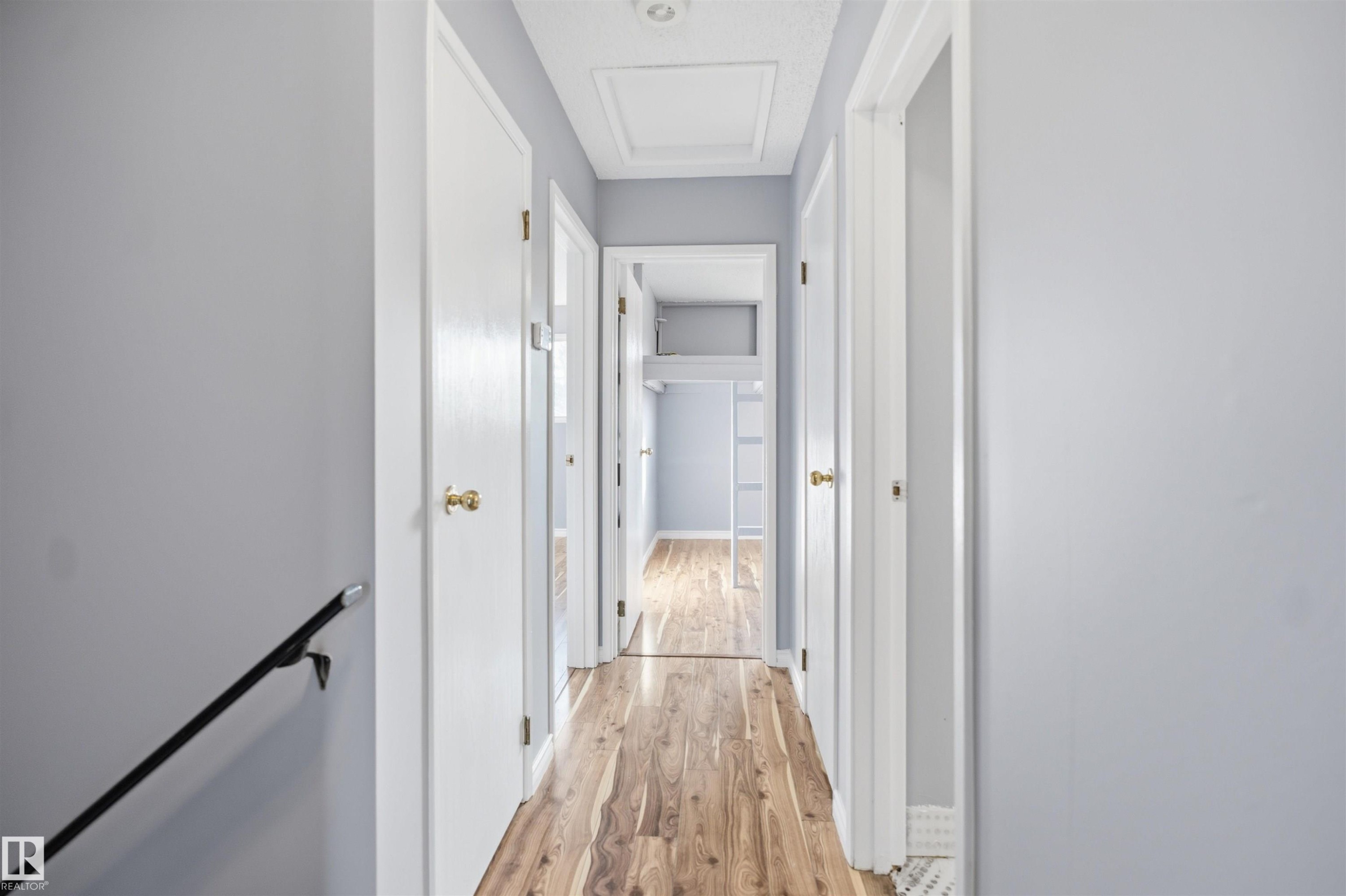 Hallway with wood-finish flooring, light gray walls, white doors with brass hardware, and a ceiling-mounted light fixture - 3432 Hill View Crescent Nw, Edmonton, AB - Indoor Photo Showing Other Room