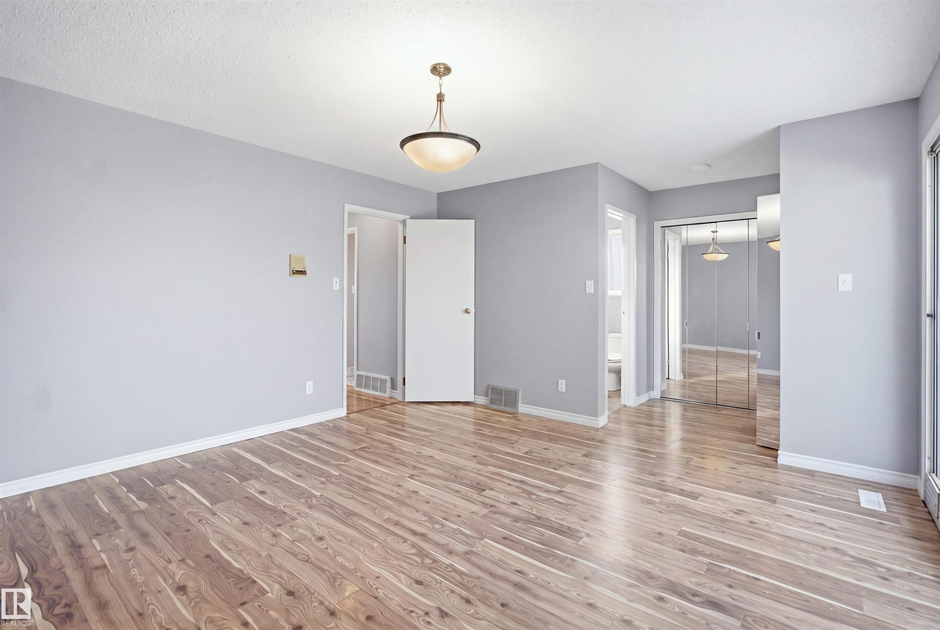 Wood-finish flooring, overhead dome light fixture, white trim, and mirrored closet doors - 3432 Hill View Crescent Nw, Edmonton, AB - Indoor Photo Showing Other Room