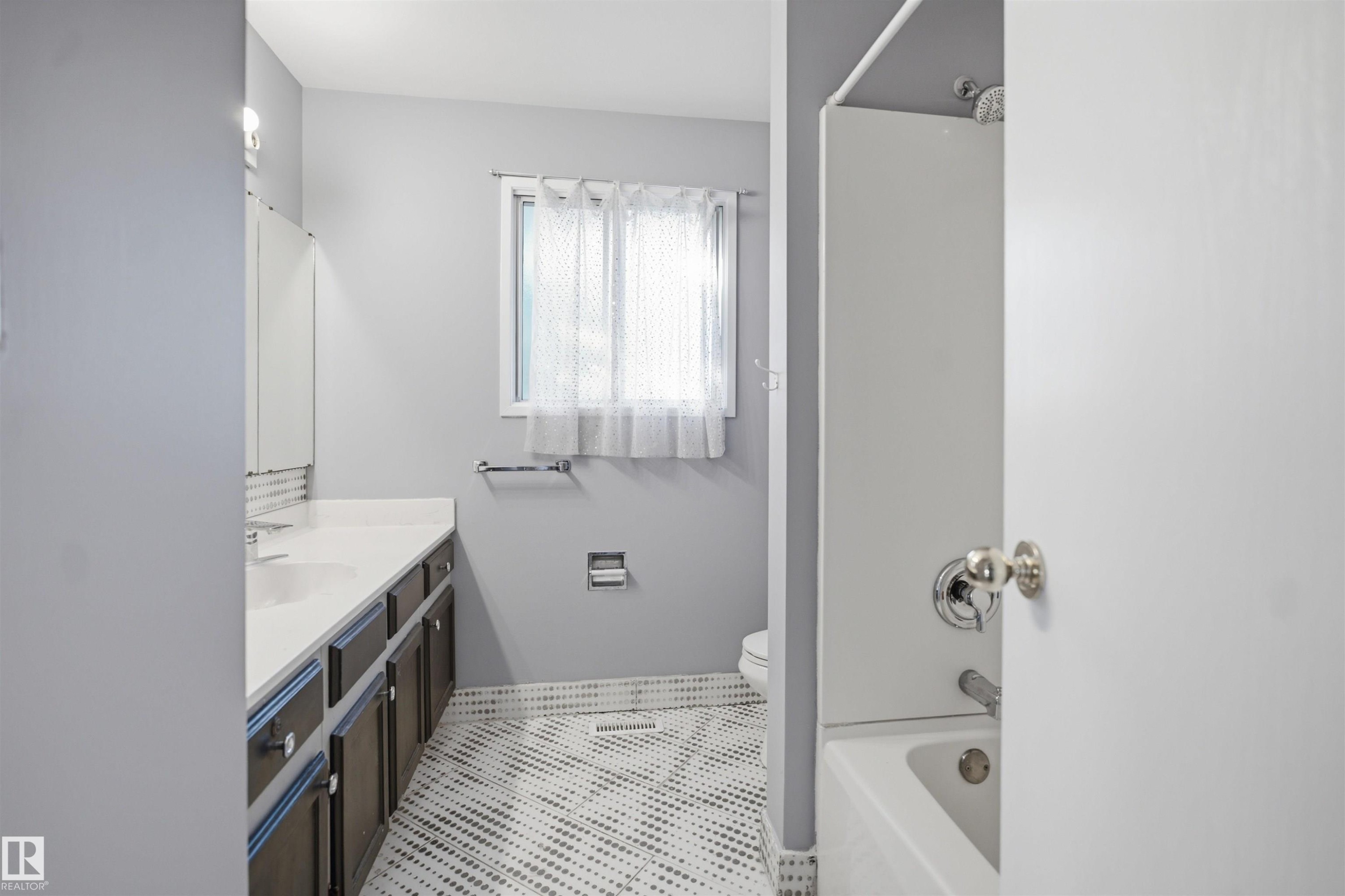 Bathroom featuring a white vanity countertop, dark wood-finish cabinetry, a window with privacy covering, and patterned floor tile - 3432 Hill View Crescent Nw, Edmonton, AB - Indoor Photo Showing Bathroom