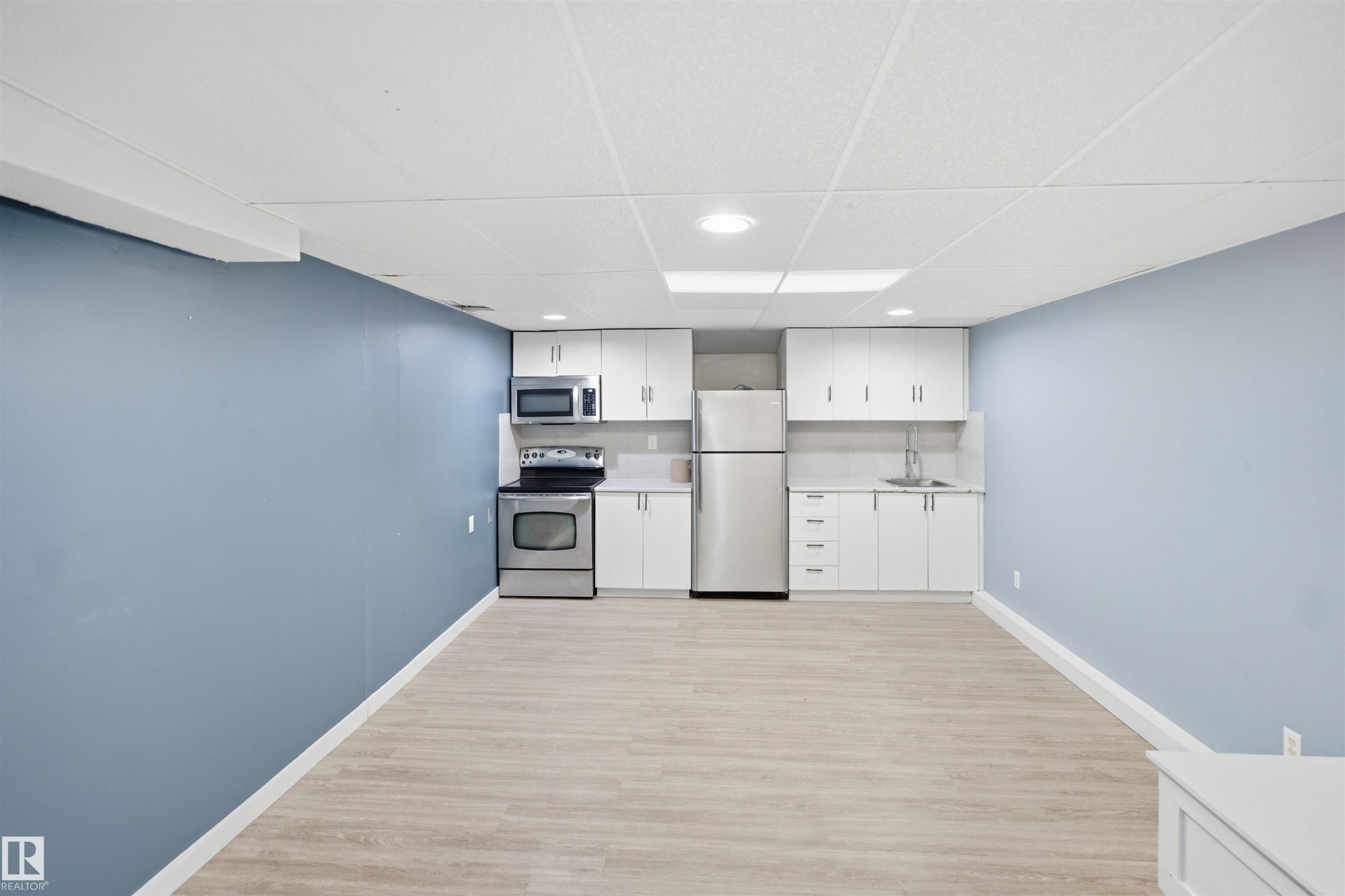Compact kitchen featuring stainless steel appliances, white cabinetry, light-toned countertops, and a stainless steel sink - 3432 Hill View Crescent Nw, Edmonton, AB - Indoor