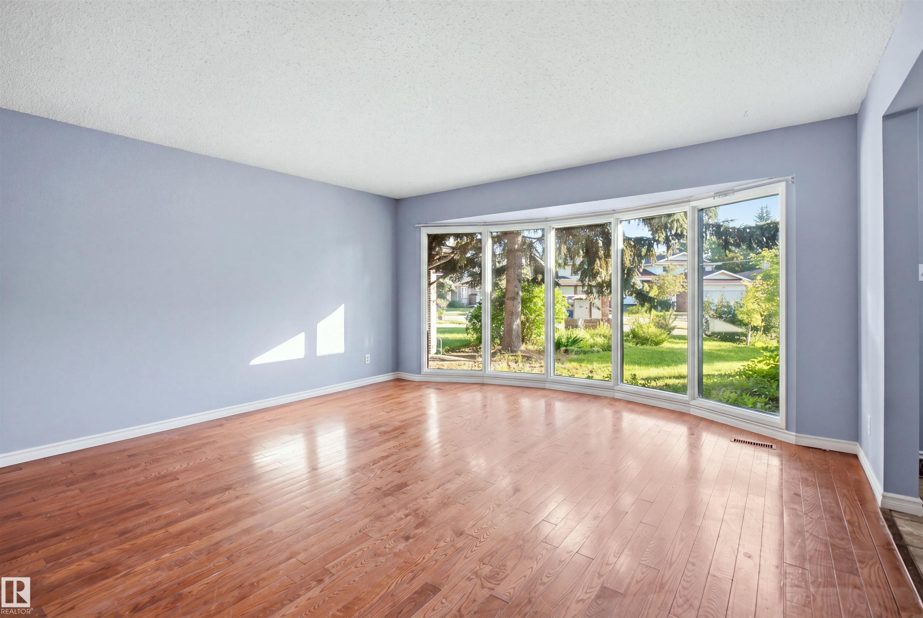 Curved bay window, wood-finish flooring, white trim, and light blue walls - 3432 Hill View Crescent Nw, Edmonton, AB - Indoor Photo Showing Other Room