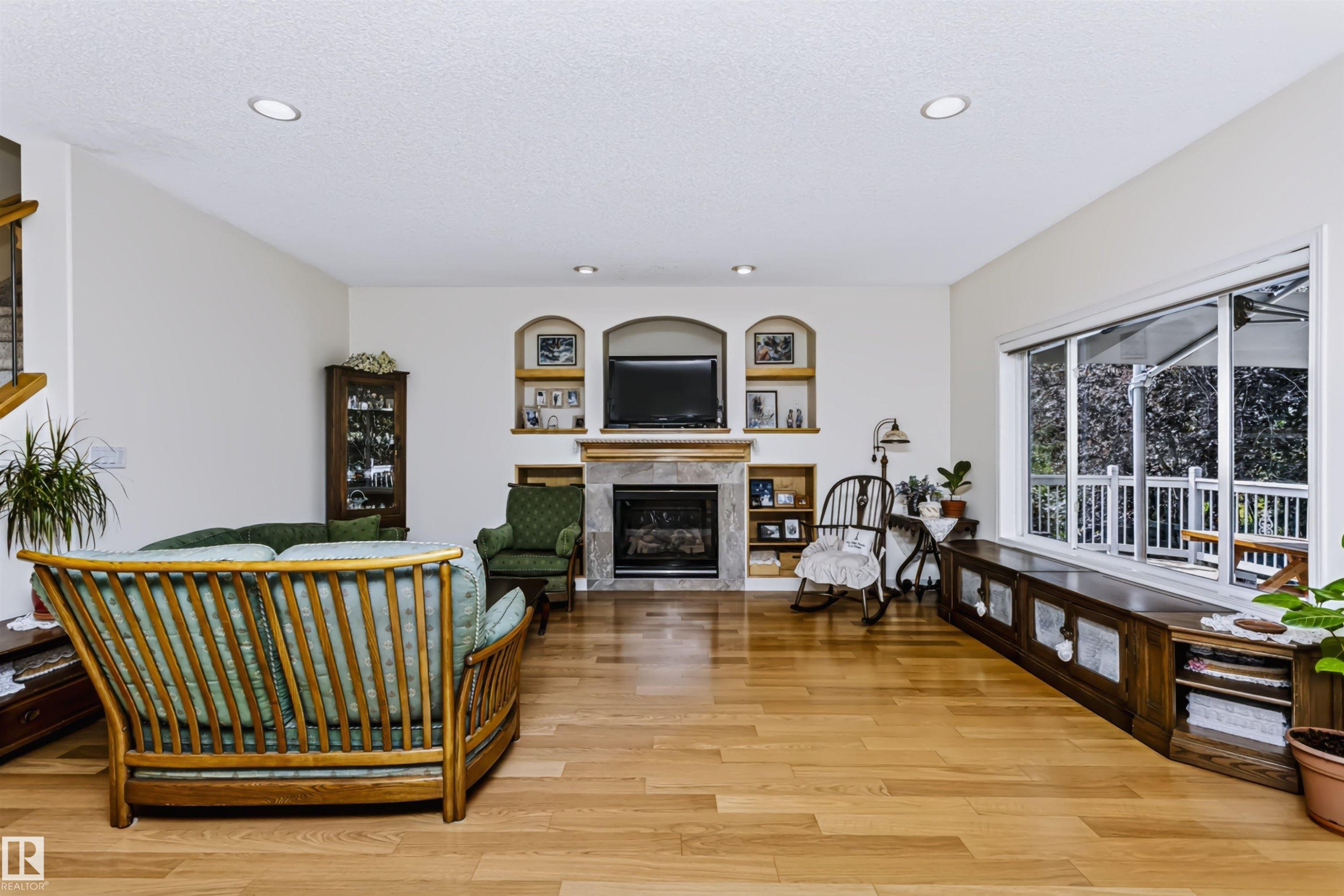 Hardwood flooring throughout, recessed ceiling lighting, stone-clad fireplace with mantel, built-in arched shelving, and large picture windows - 1720 Robertson Place Sw, Edmonton, AB - Indoor With Fireplace