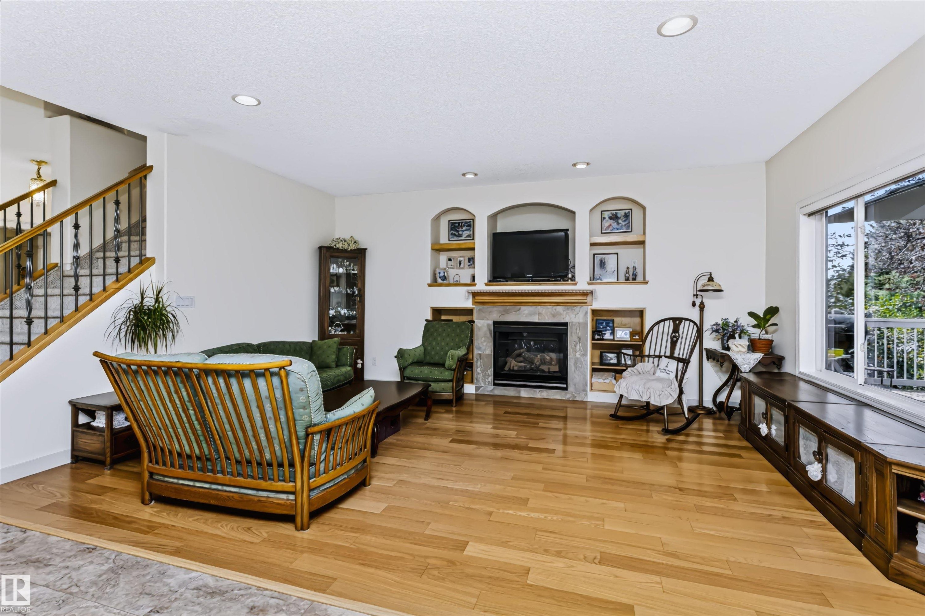 Hardwood flooring throughout, stone-clad fireplace, integrated shelving, and large window with built-in storage - 1720 Robertson Place Sw, Edmonton, AB - Indoor Photo Showing Living Room With Fireplace