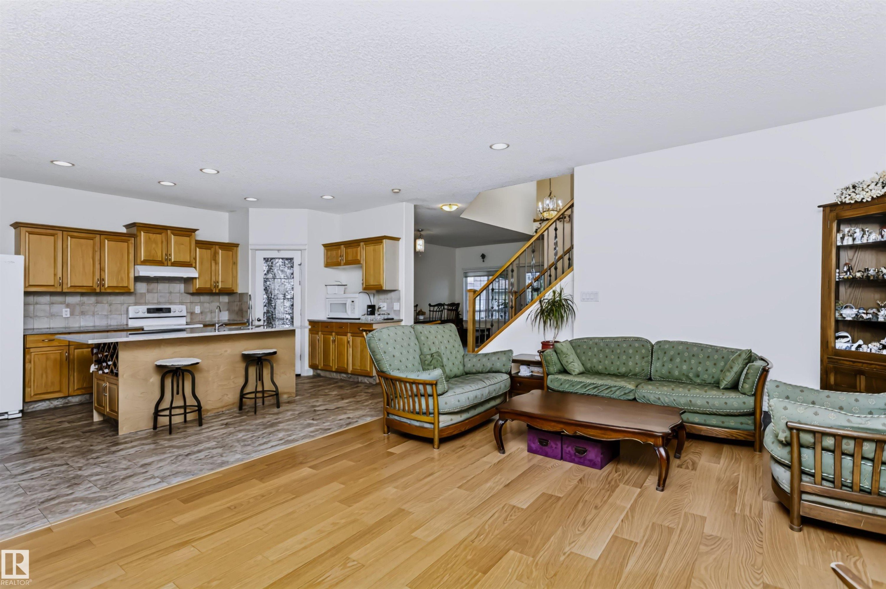 Open-concept living area with wood-finish flooring, recessed lighting, and a prominent staircase with wood railings - 1720 Robertson Place Sw, Edmonton, AB - Indoor Photo Showing Other Room
