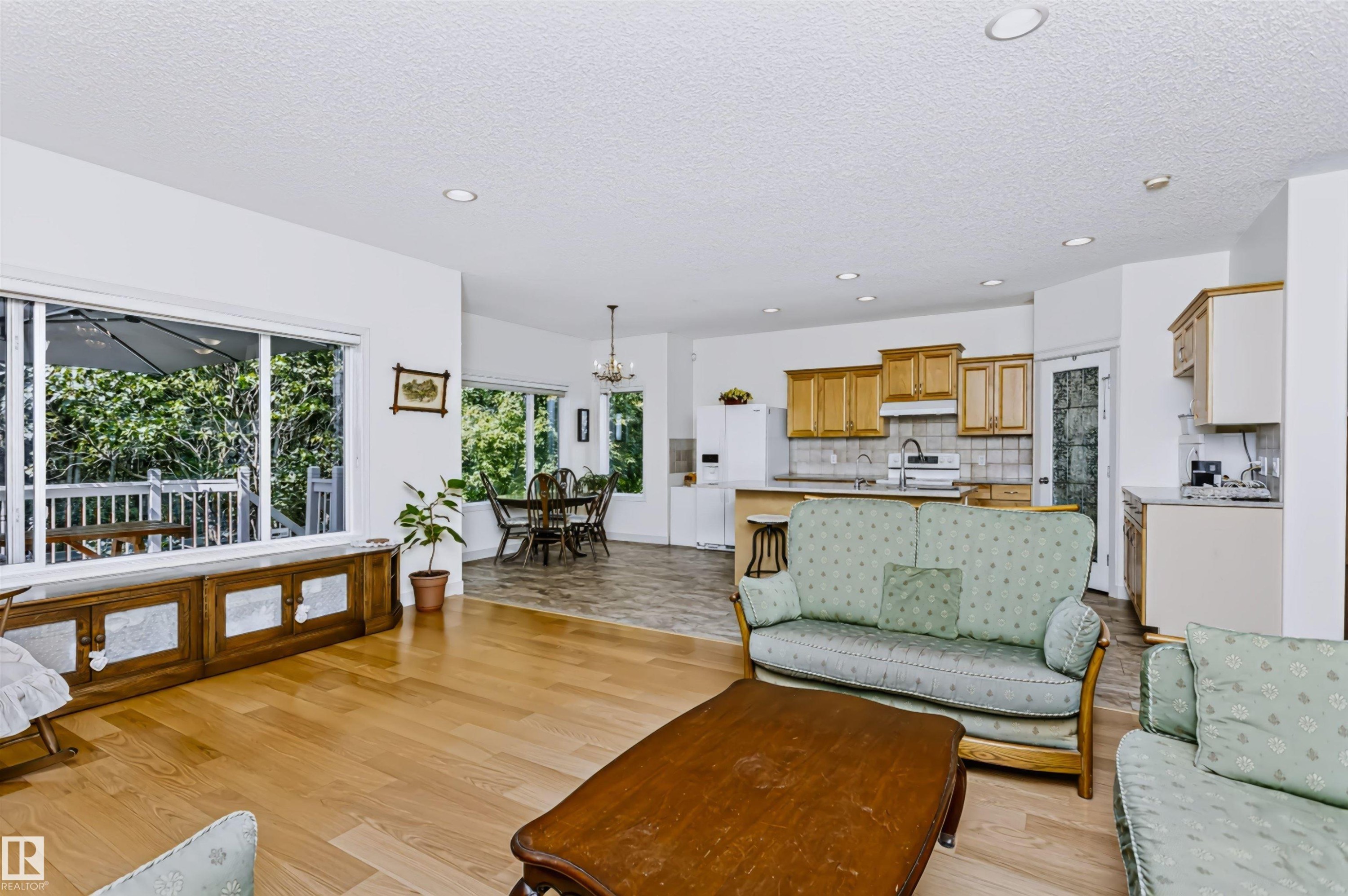 Hardwood flooring, sliding glass door leading to an outdoor deck, recessed lighting, kitchen with wood cabinetry and tile backsplash, and a dining area with a chandelier - 1720 Robertson Place Sw, Edmonton, AB - Indoor Photo Showing Living Room