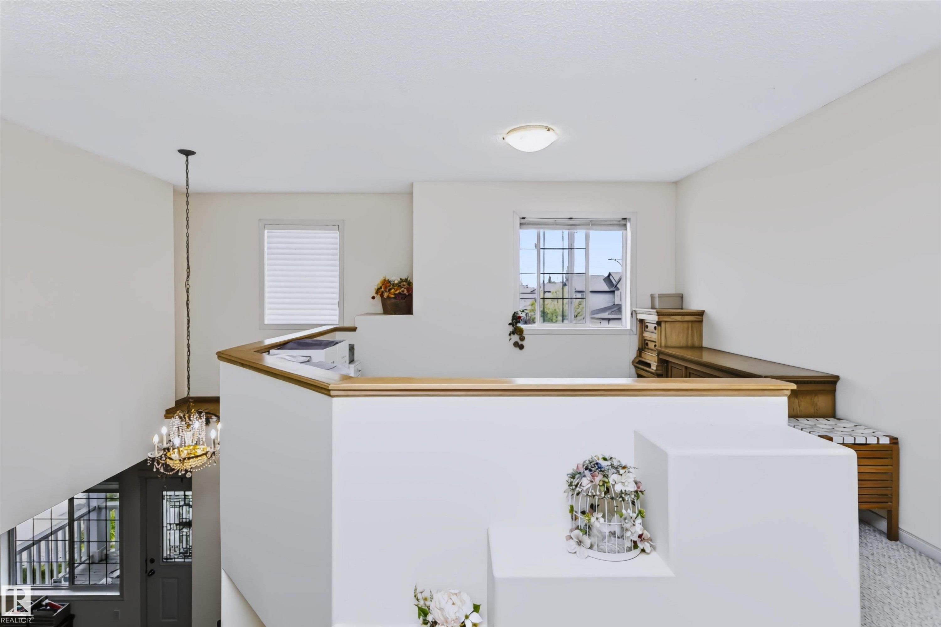 Upper-level landing with wood-finish railing, a window with grid detailing, and a flush-mount ceiling light - 1720 Robertson Place Sw, Edmonton, AB - Indoor Photo Showing Other Room
