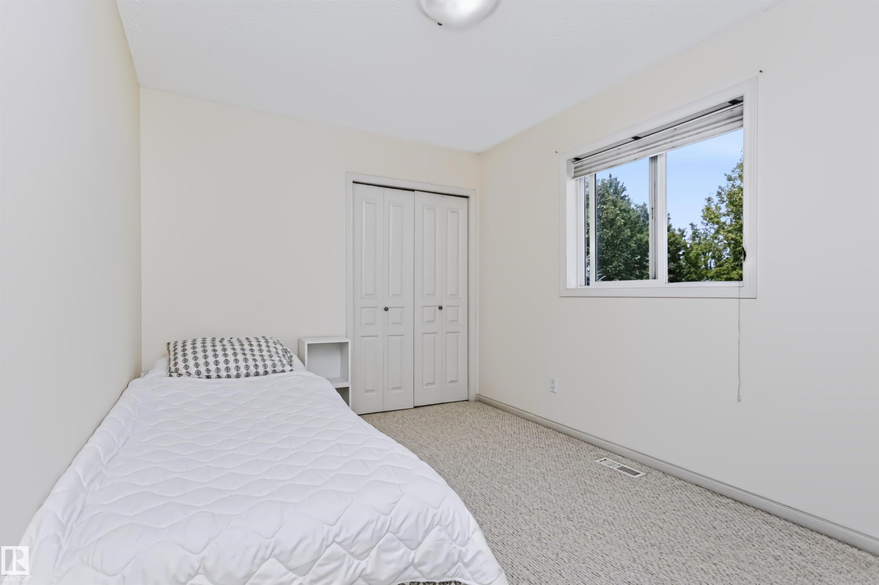 Neutral wall color, light-toned carpeting, window with natural light, and a built-in closet with bifold doors - 1720 Robertson Place Sw, Edmonton, AB - Indoor Photo Showing Bedroom