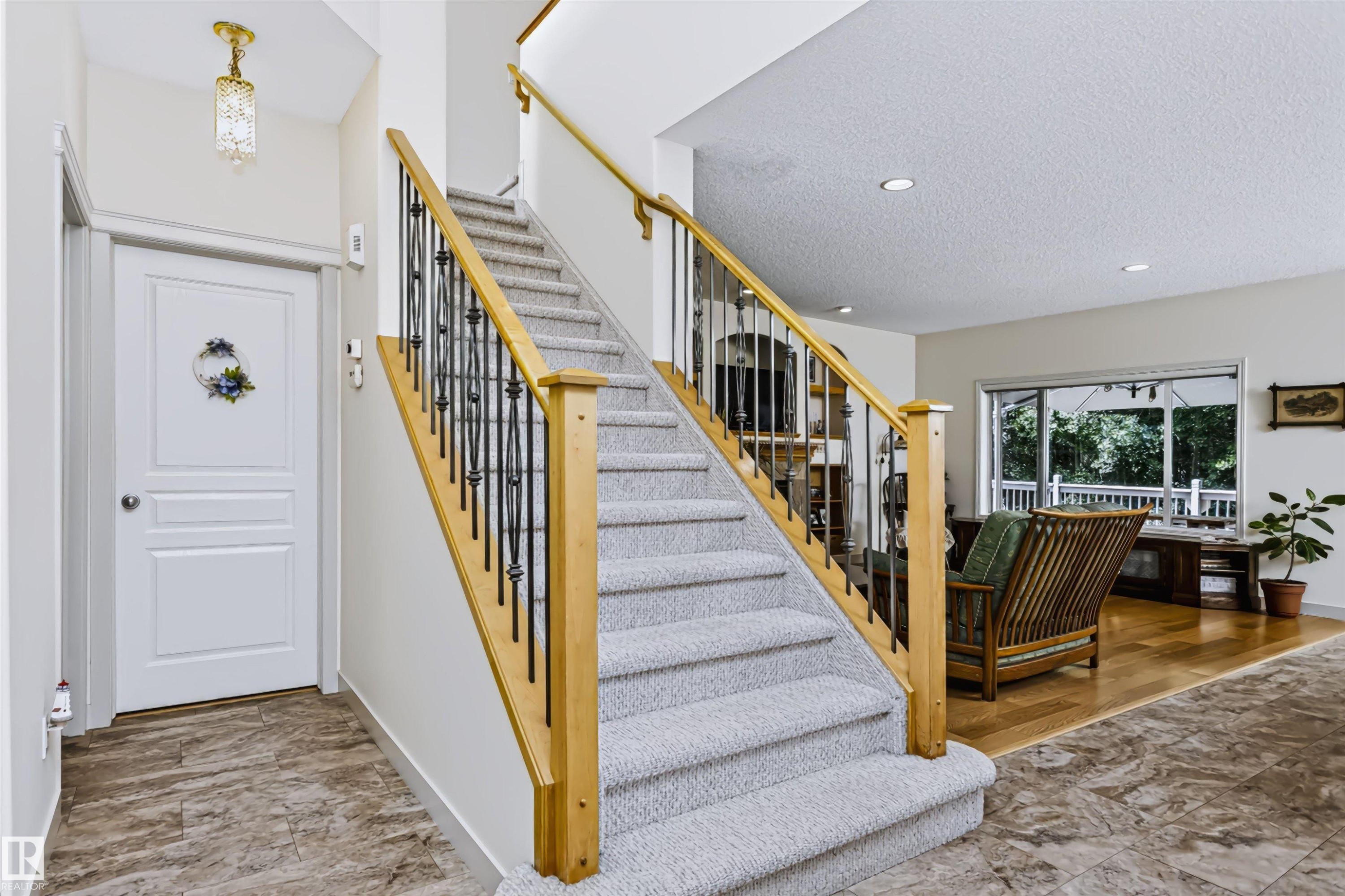 Carpeted staircase with wood newel posts and wrought iron balusters, recessed ceiling lighting, wood-finish flooring, and a glass-paneled exterior door - 1720 Robertson Place Sw, Edmonton, AB - Indoor Photo Showing Other Room