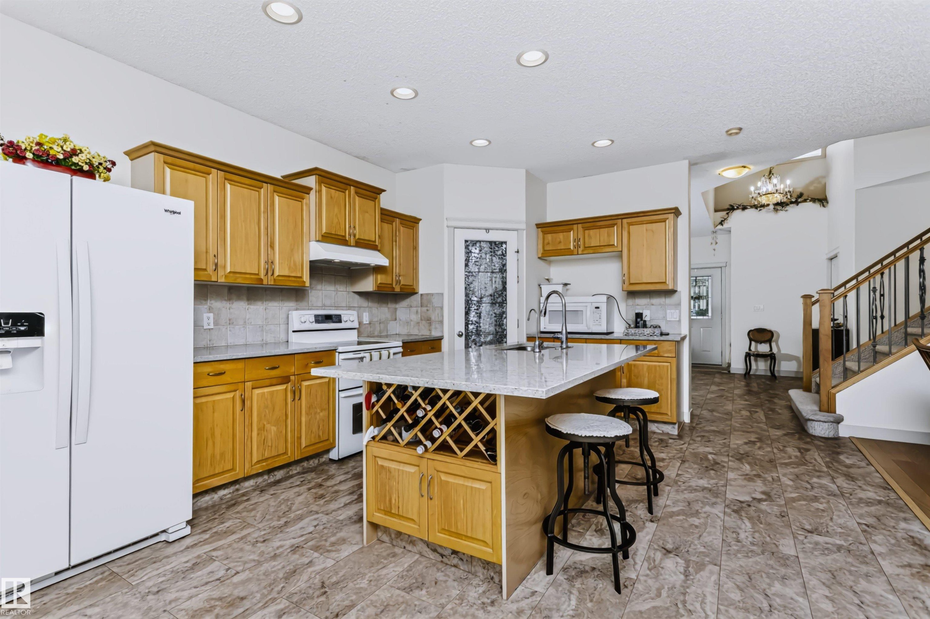 Kitchen featuring wood cabinetry, a center island with integrated wine storage, a tile backsplash, and recessed lighting - 1720 Robertson Place Sw, Edmonton, AB - Indoor Photo Showing Kitchen