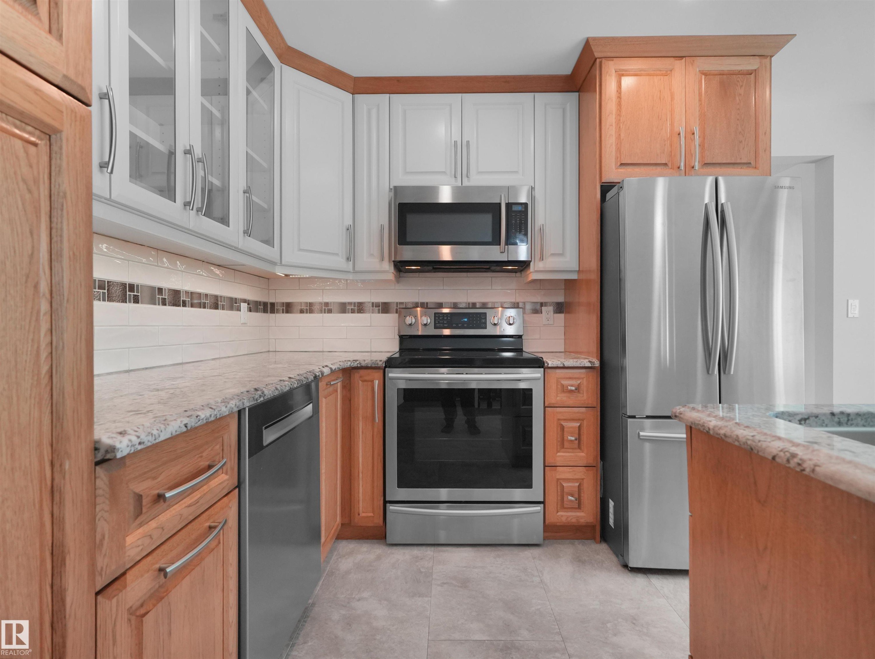 Modern kitchen featuring mixed cabinetry in warm wood and crisp white finishes, stainless steel appliances including a French-door refrigerator and convection range, granite countertops, and a subway tile backsplash with decorative border accent - 7357 18 Avenue Nw, Edmonton, AB - Indoor Photo Showing Kitchen