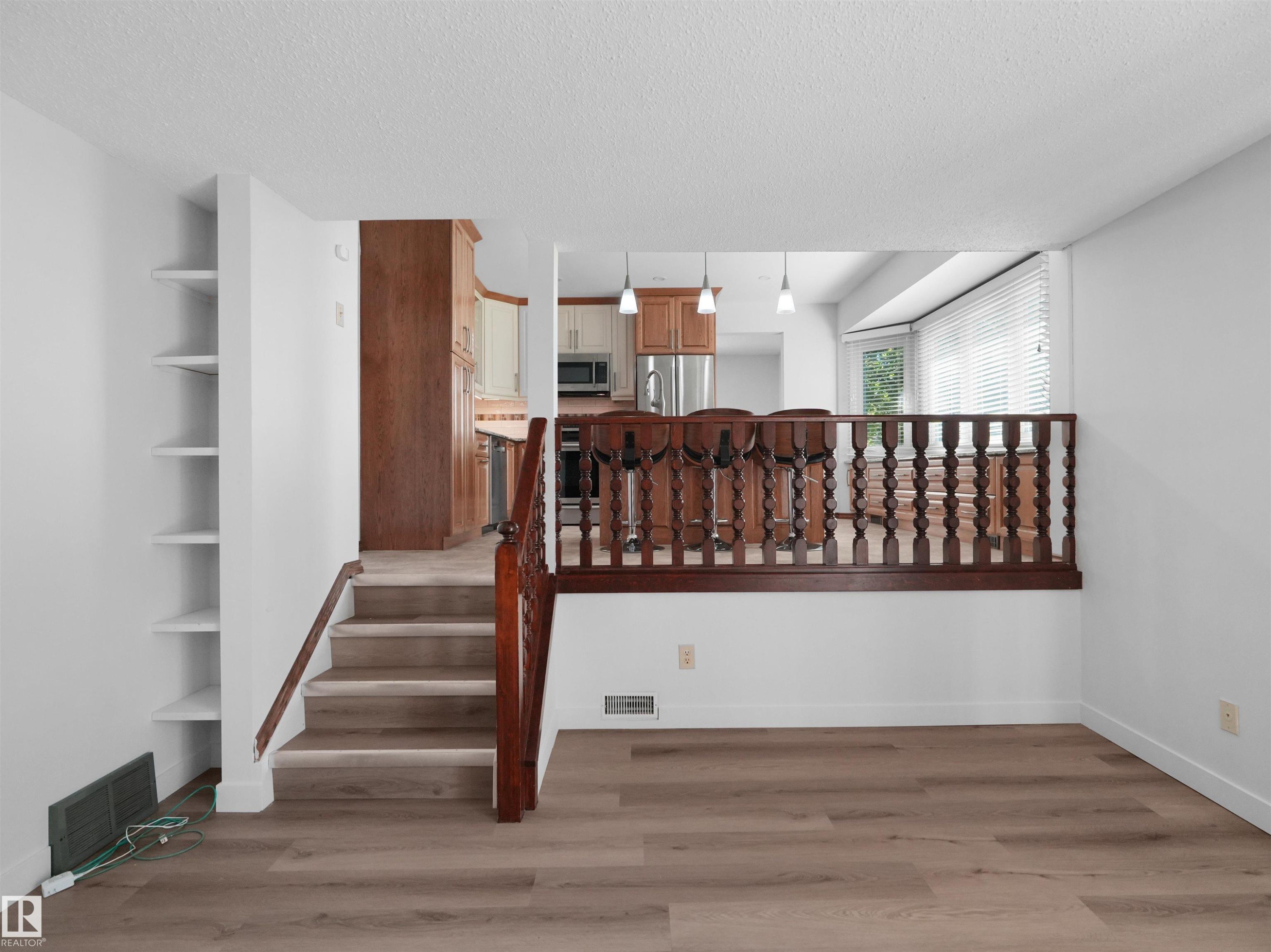 Wood-finish flooring, built-in shelving, wood staircase, and an open-concept kitchen with pendant lighting - 7357 18 Avenue Nw, Edmonton, AB - Indoor Photo Showing Other Room
