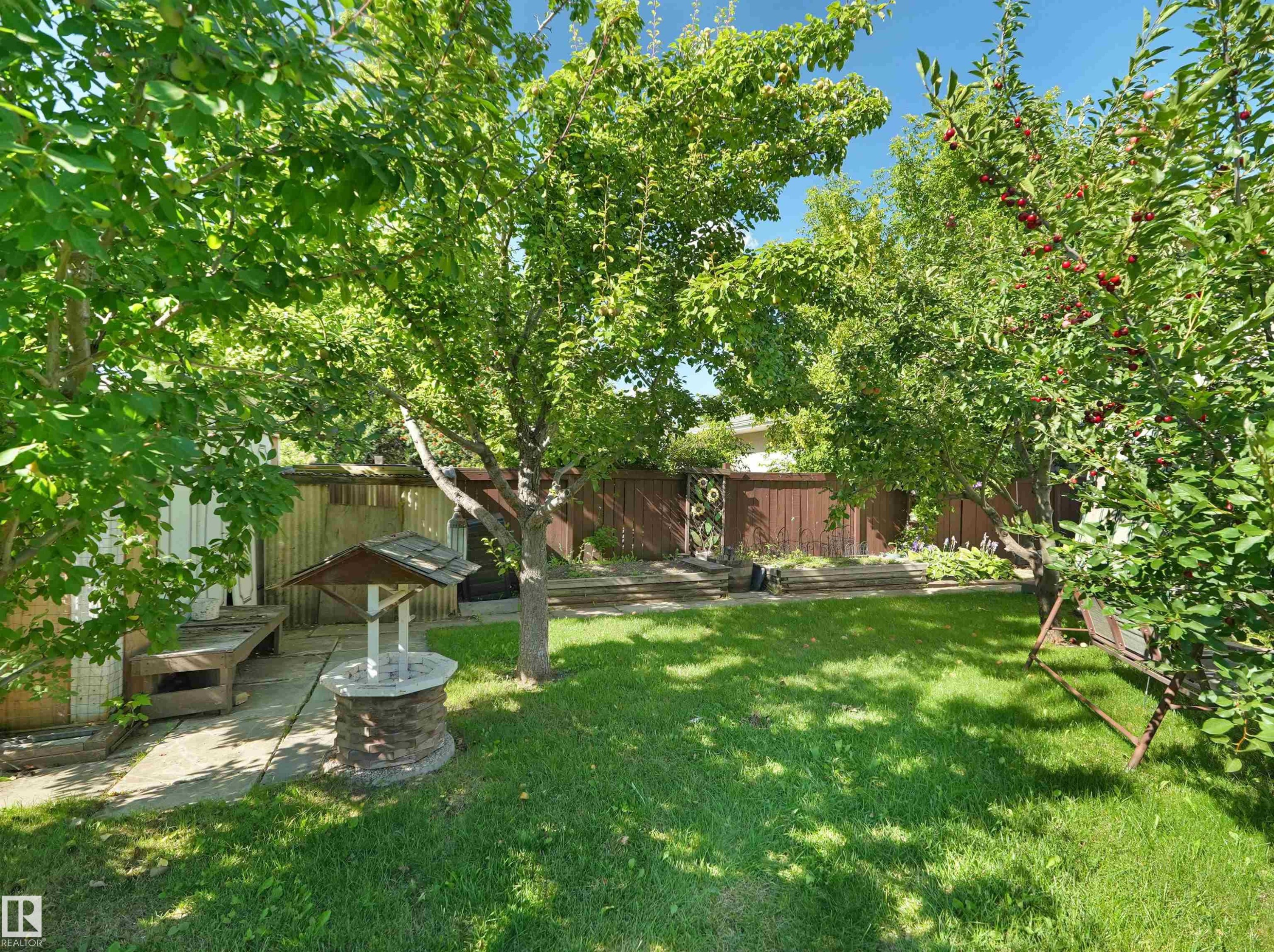 Expansive backyard featuring a manicured lawn, established trees, and a stone-clad well feature - 7357 18 Avenue Nw, Edmonton, AB - Outdoor