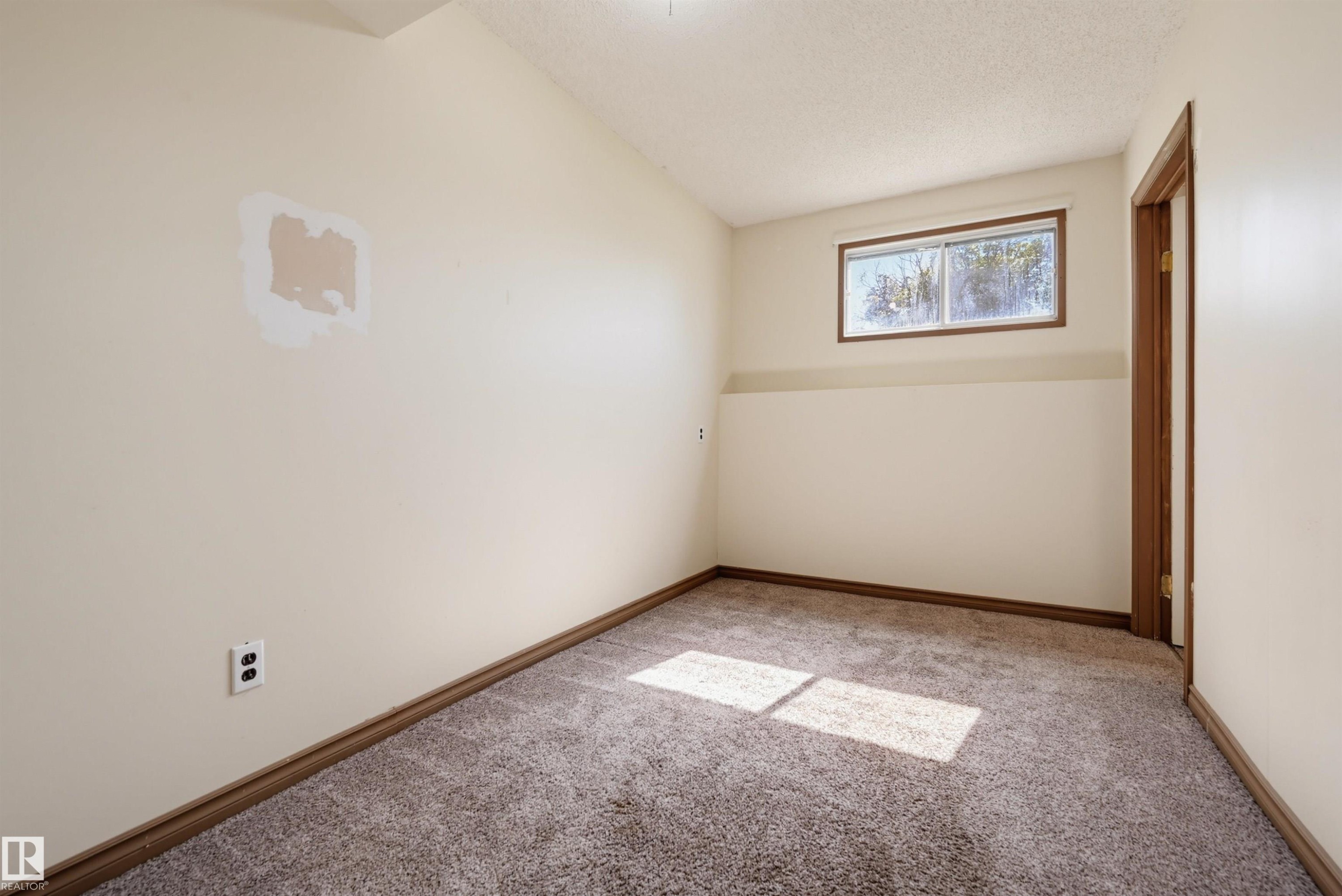 Carpeted room featuring a window with wood-frame trim and a wood-paneled door frame - 6768 39 Avenue Nw, Edmonton, AB - Indoor Photo Showing Other Room
