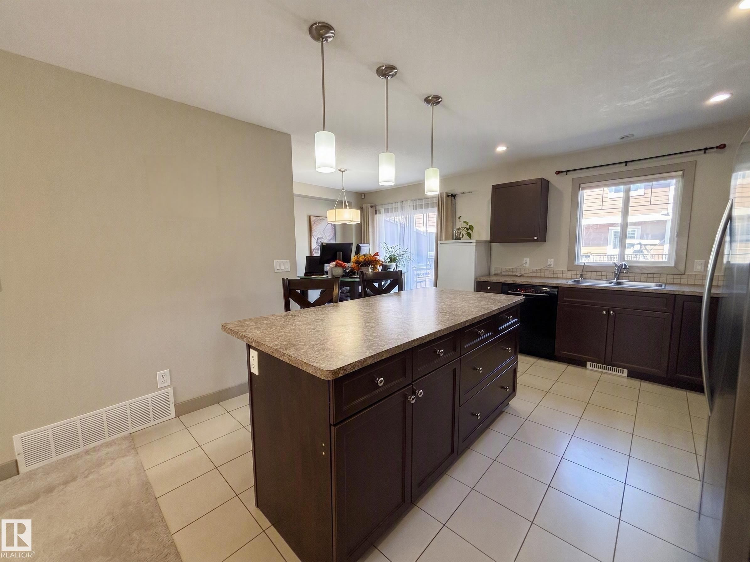 Kitchen featuring a center island, dark wood-finish cabinetry, tile flooring, and pendant lighting - #29 1150 Windermere Wy Sw, Edmonton, AB
