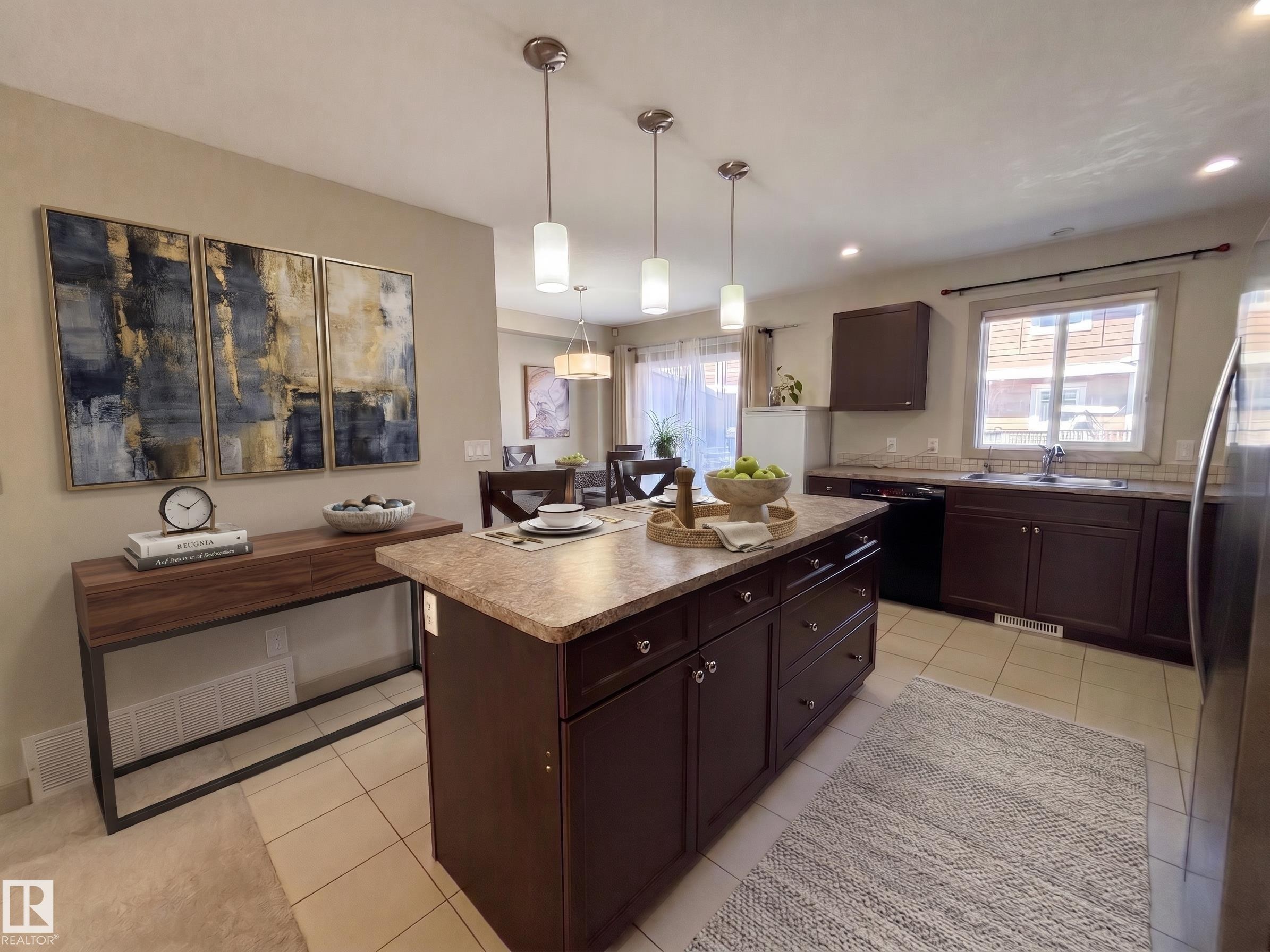 Kitchen island with pendant lighting, dark wood-finish cabinetry, tile flooring, and a dining area beyond - #29 1150 Windermere Wy Sw, Edmonton, AB