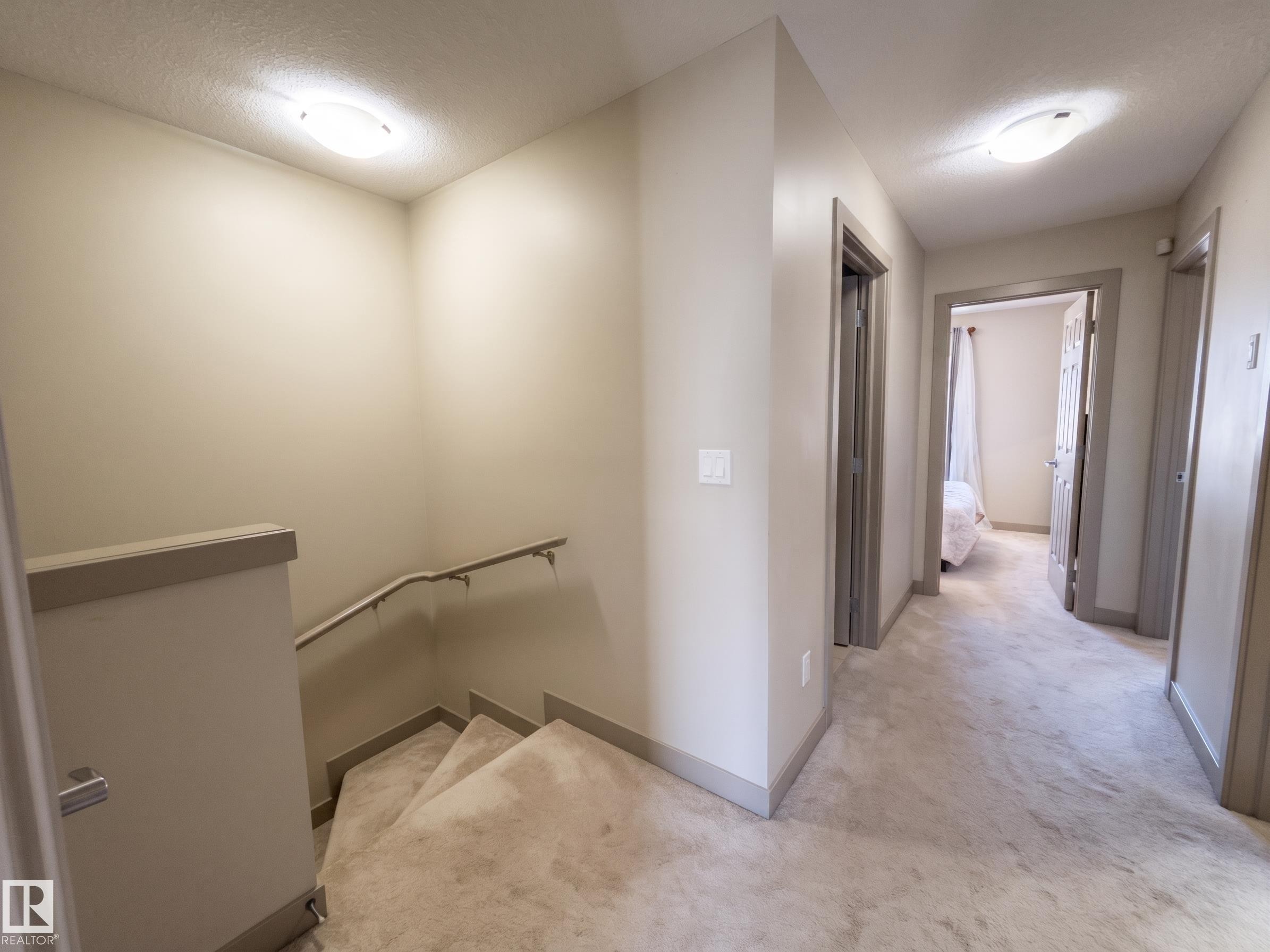 Hallway with neutral wall paint, overhead flush mount lighting, and gray trim - #29 1150 Windermere Wy Sw, Edmonton, AB