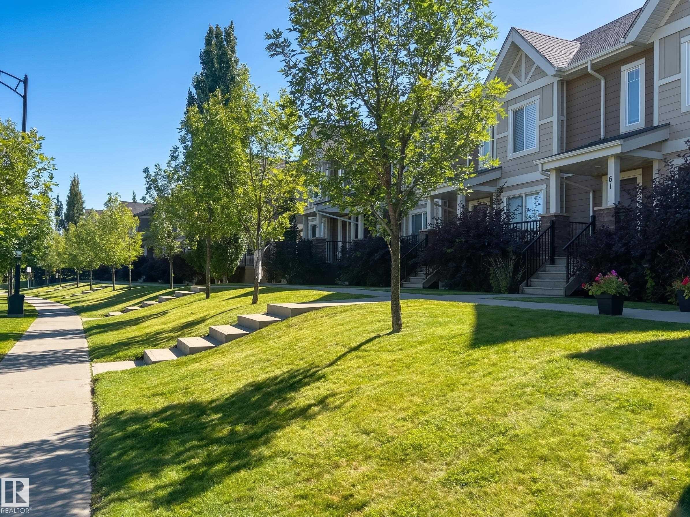 Townhome exterior with a pitched roof, siding facade, covered entry, and front porch with railings - #29 1150 Windermere Wy Sw, Edmonton, AB