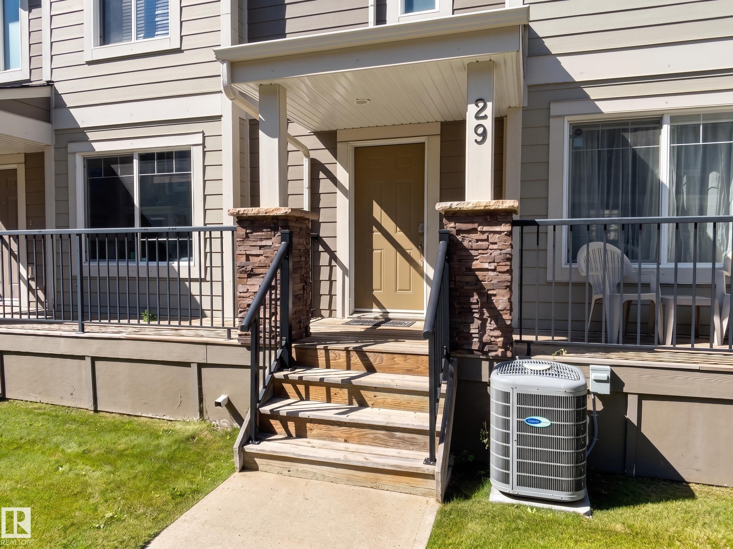 Exterior featuring horizontal siding, a covered porch, stone veneer column accents, a security railing, and an outdoor HVAC unit - #29 1150 Windermere Wy Sw, Edmonton, AB