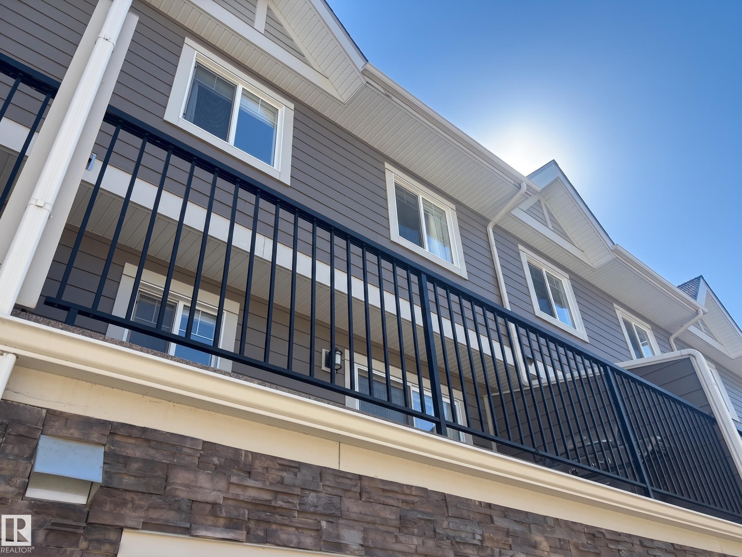 Exterior featuring horizontal siding, decorative gable vents, white window trim, dark metal balcony railing, and stone-look facade - #29 1150 Windermere Wy Sw, Edmonton, AB