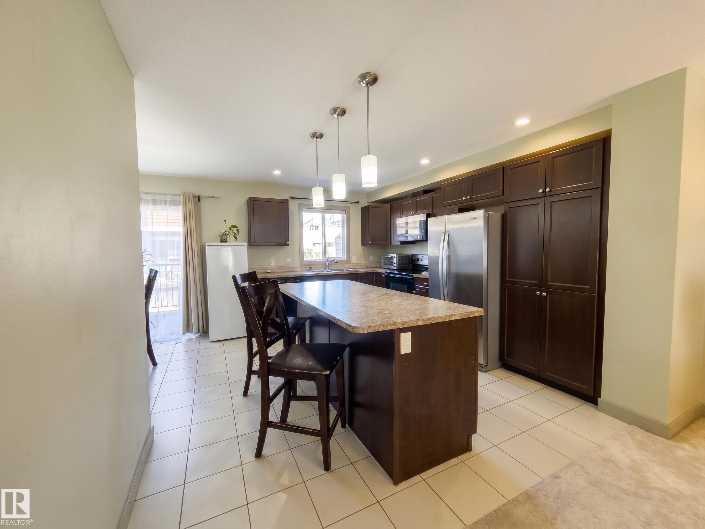 Kitchen featuring a center island, pendant lighting, recessed lighting, tile flooring, and dark wood cabinetry - #29 1150 Windermere Wy Sw, Edmonton, AB