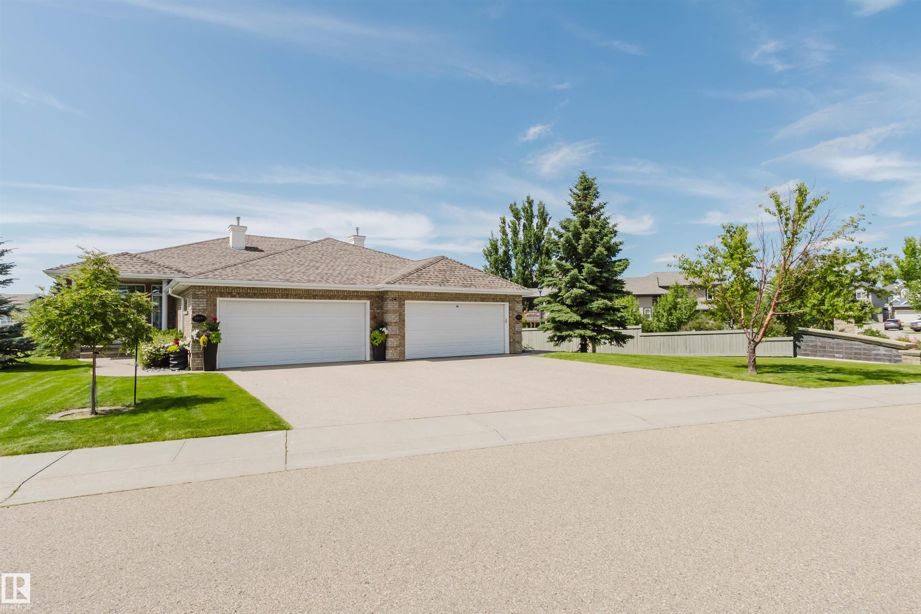 Brick exterior residence featuring a multi-car garage, mature landscaping, and an expansive driveway - 6604 Sandin Cove Nw, Edmonton, AB - Outdoor