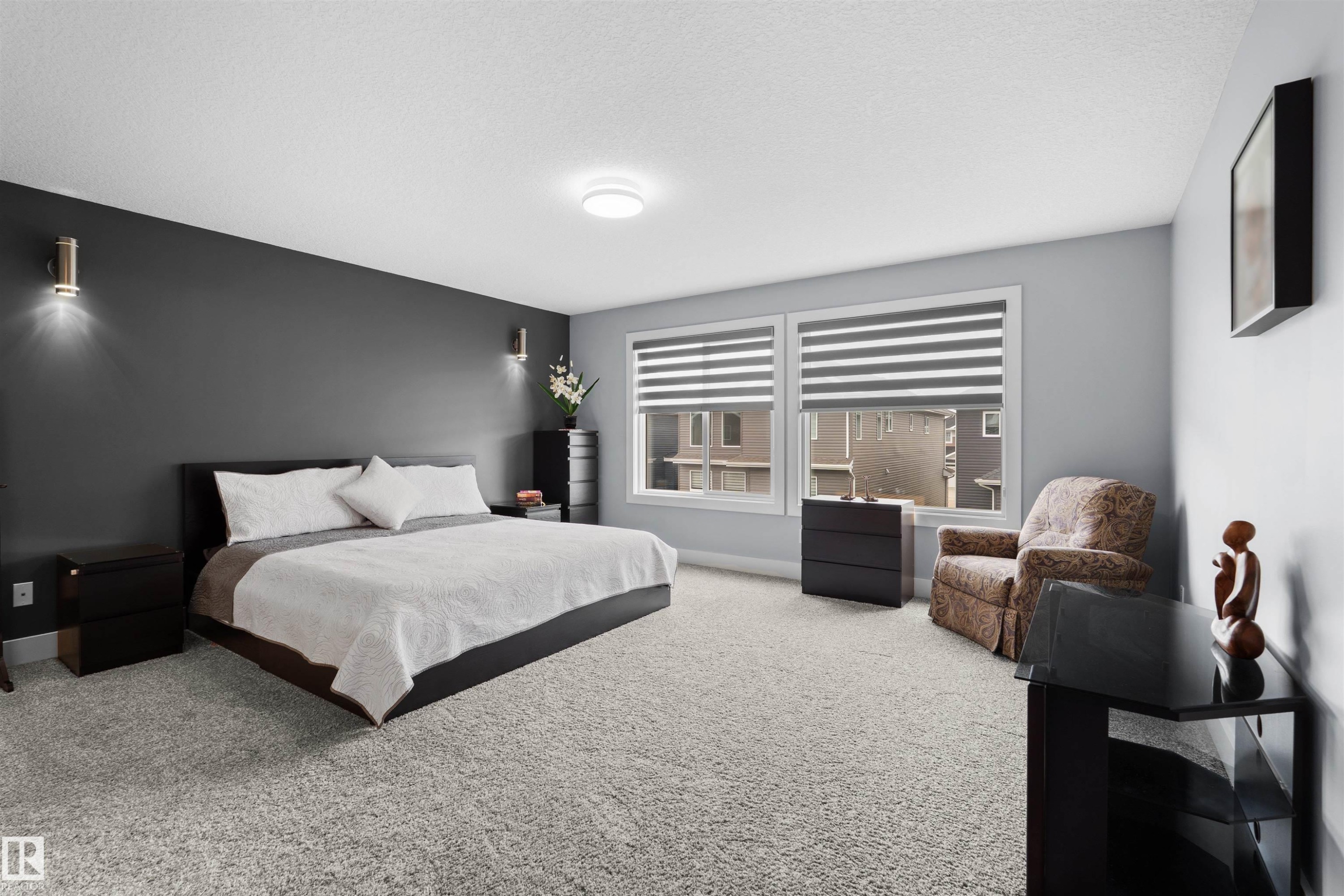 Carpeted bedroom featuring dual windows with horizontal blinds, a ceiling-mounted light fixture, and two wall-mounted sconces - 16327 17 Avenue Sw, Edmonton, AB - Indoor Photo Showing Bedroom