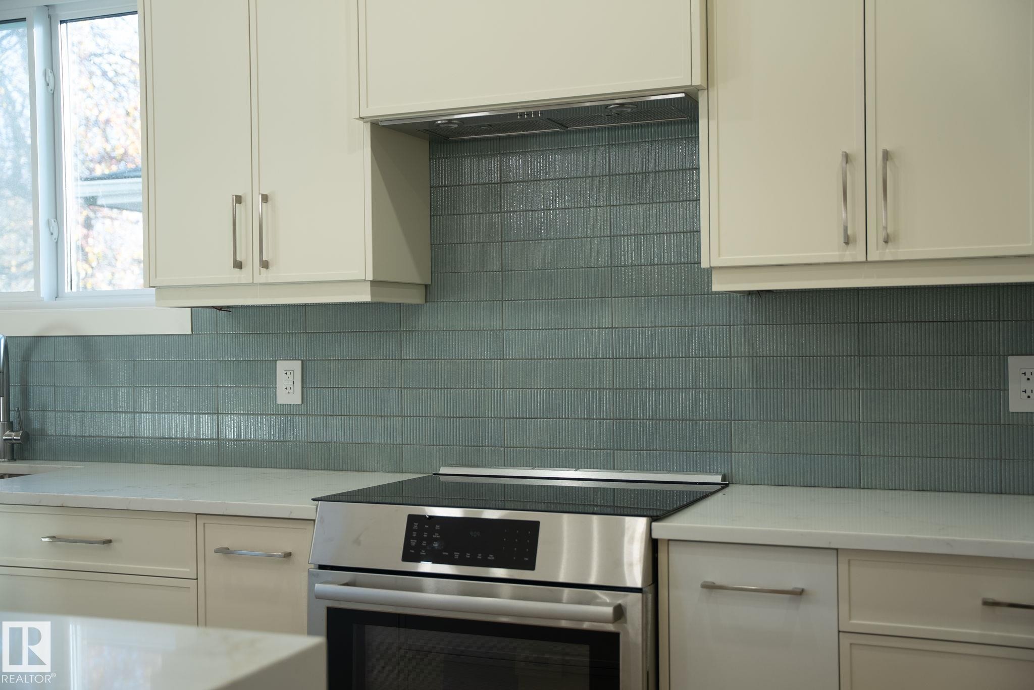 White cabinetry, light countertops, integrated stainless steel range, and a textured blue tile backsplash - 9736 73 Avenue Nw, Edmonton, AB