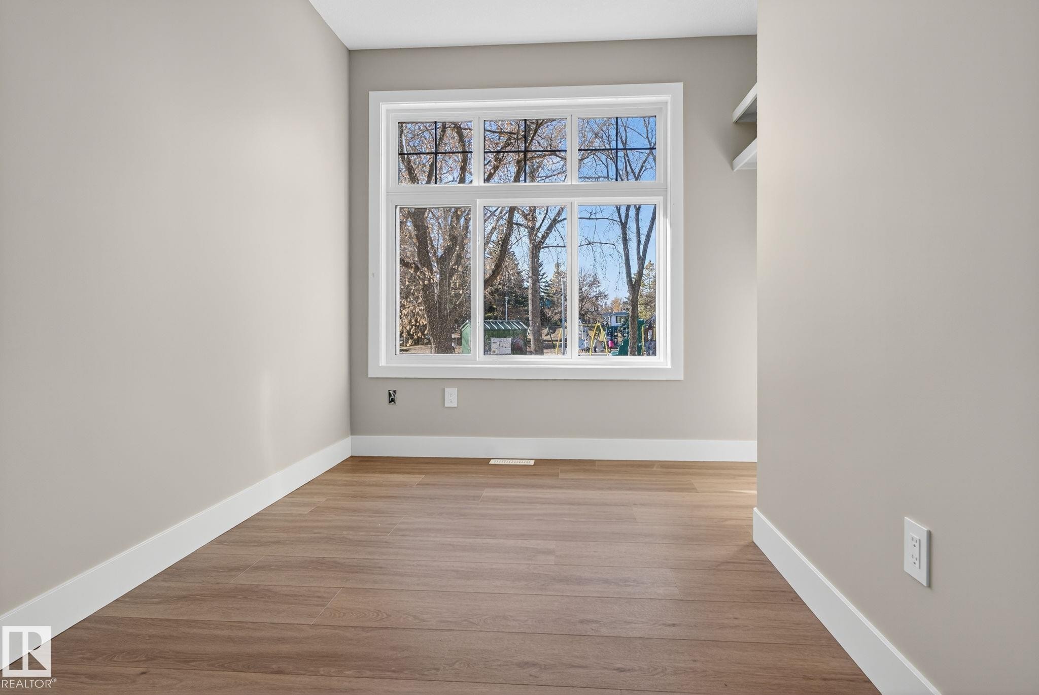 Wood-finish flooring, neutral wall tones, large multi-pane window, white window trim, and white baseboards - 9736 73 Avenue Nw, Edmonton, AB