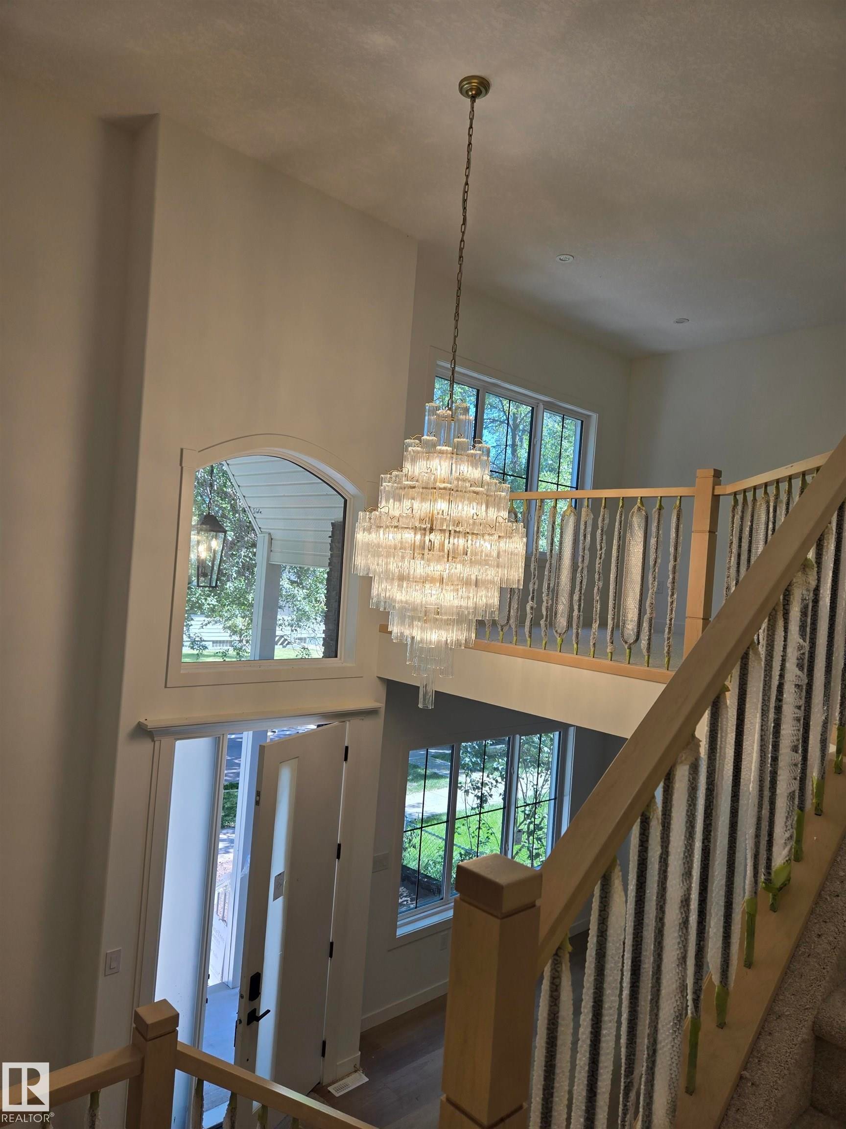 Two-story foyer with a tiered chandelier, hardwood flooring, and a grand staircase featuring wood newel posts - 9736 73 Avenue Nw, Edmonton, AB