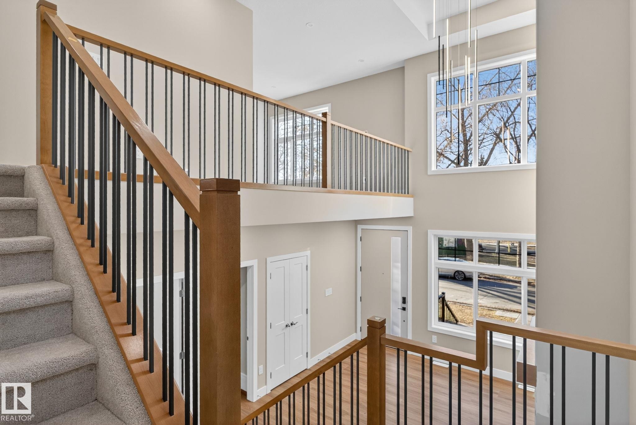 Two-story entry with a wood-finish staircase and black balusters, featuring a large multi-pane window and a modern linear chandelier - 9736 73 Avenue Nw, Edmonton, AB