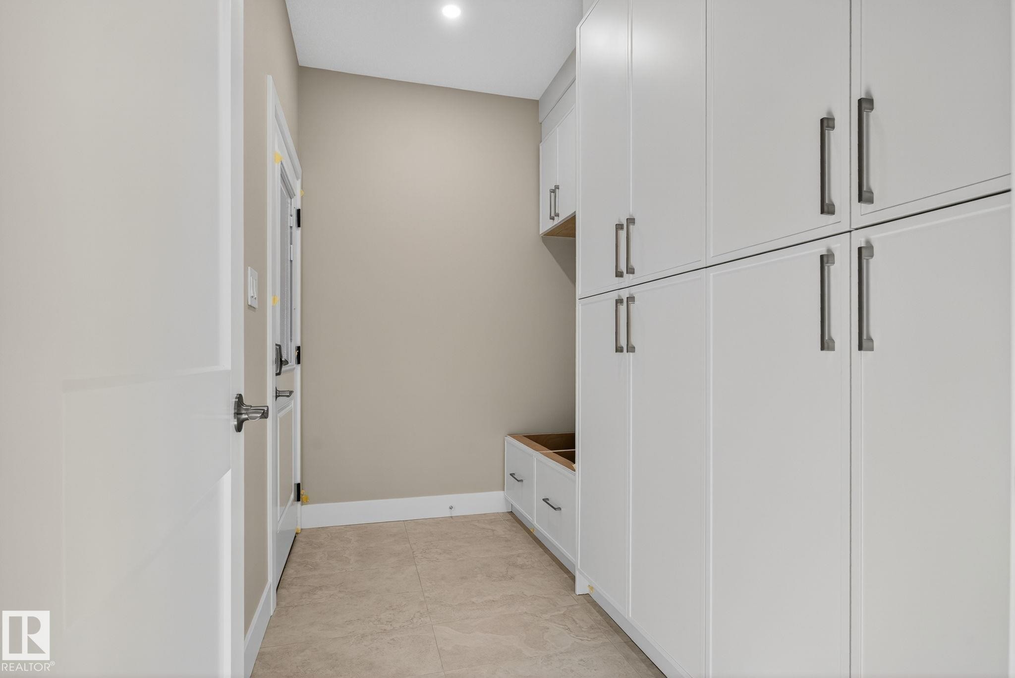 White paneled cabinetry with dark hardware, recessed lighting, built-in storage bench, and light-toned tile flooring - 9736 73 Avenue Nw, Edmonton, AB