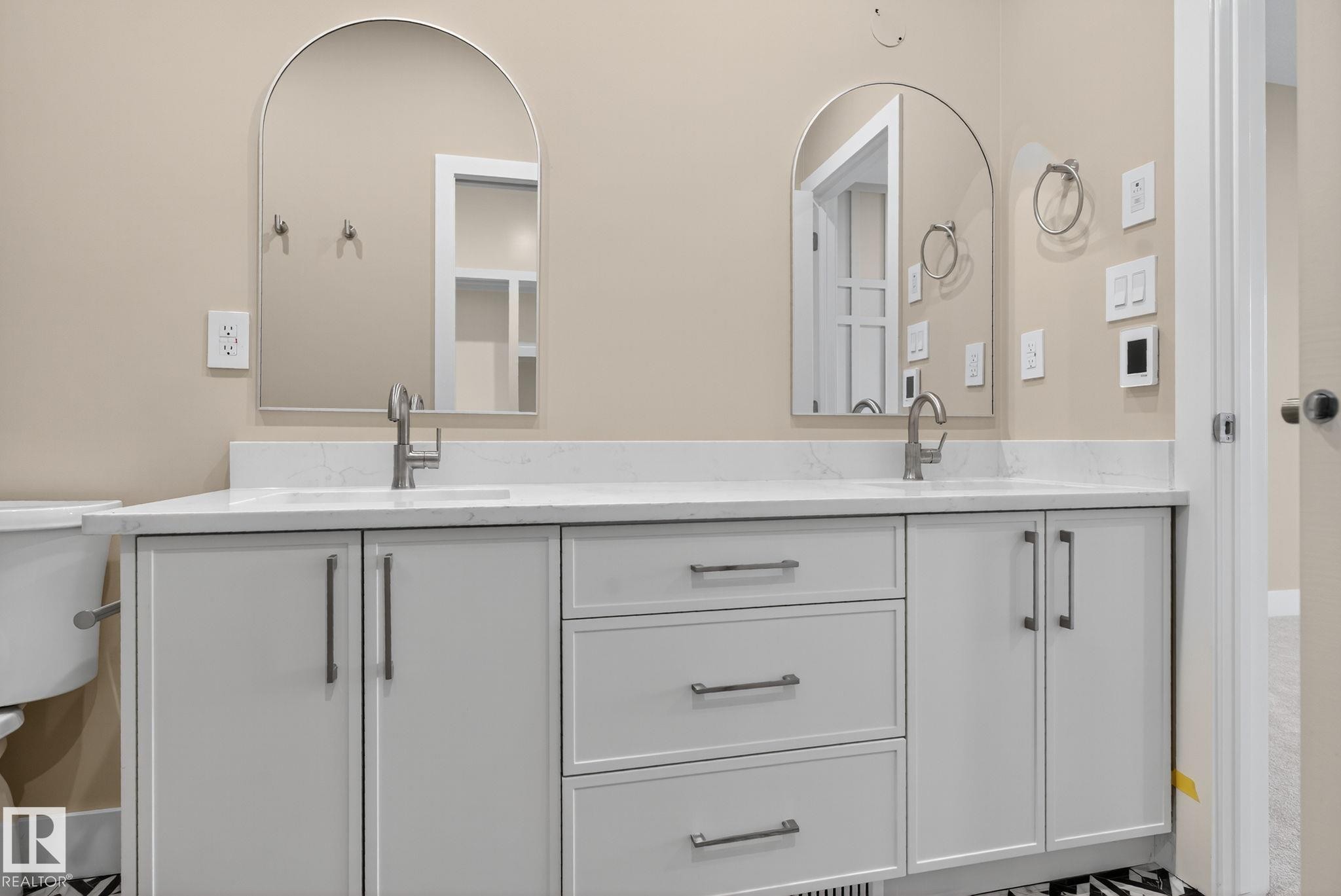 Dual arched mirrors, dual undermount sinks, white quartz countertop, custom cabinetry with brushed nickel hardware, and patterned floor tile - 9736 73 Avenue Nw, Edmonton, AB