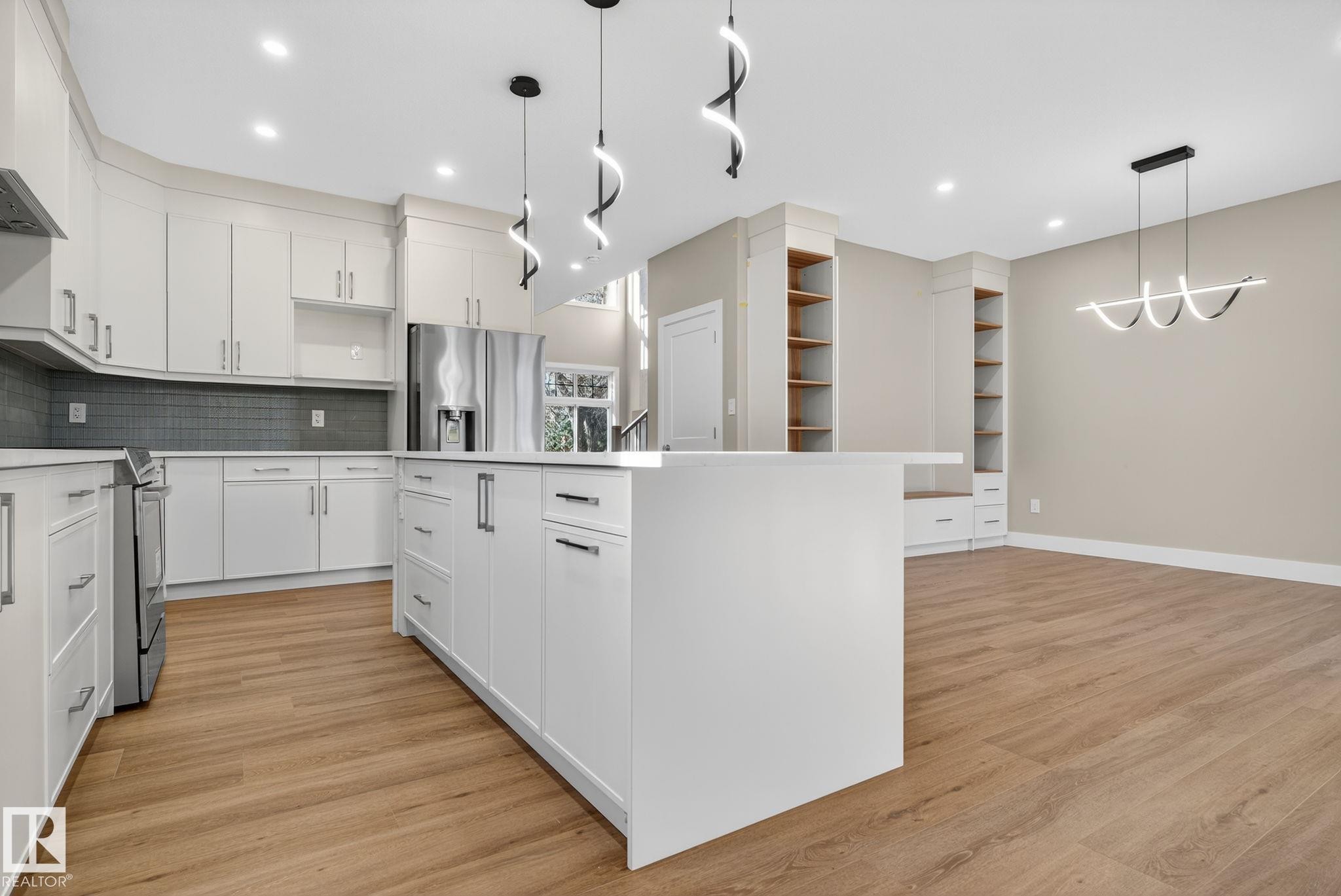 Kitchen featuring white cabinetry, a large center island, stainless steel appliances, and wood-finish flooring - 9736 73 Avenue Nw, Edmonton, AB