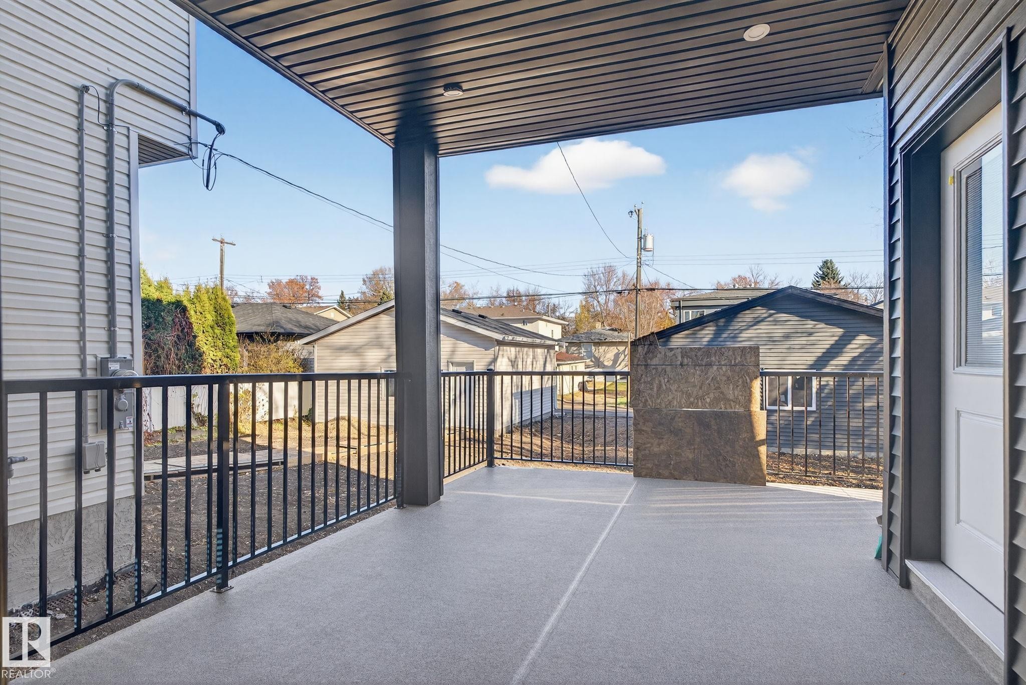 Covered patio with a light gray textured finish and black metal railings - 9736 73 Avenue Nw, Edmonton, AB