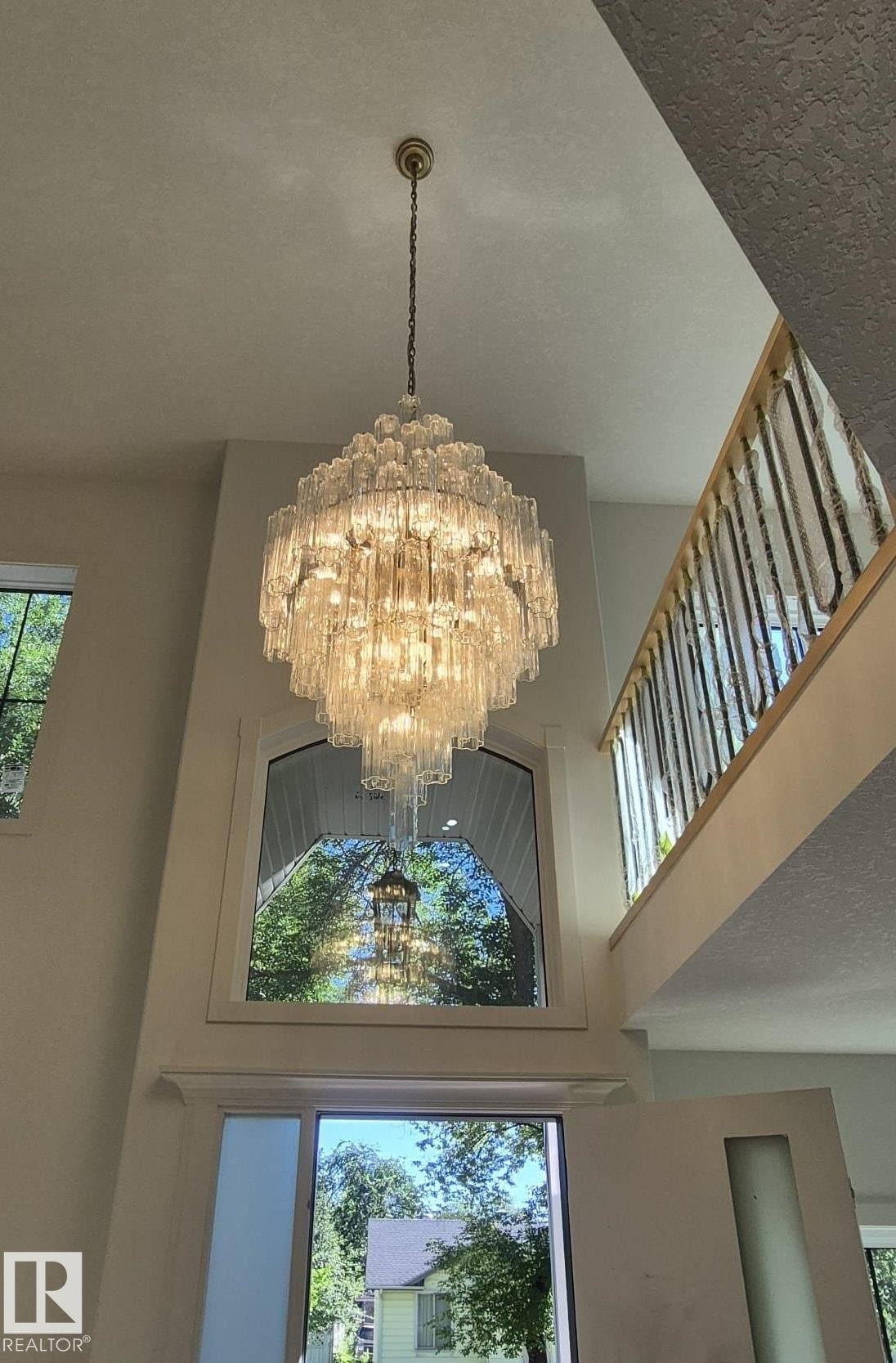 Two-story foyer featuring an ornate tiered chandelier, arched transom window, and a wood staircase with metal balusters - 9736 73 Avenue Nw, Edmonton, AB
