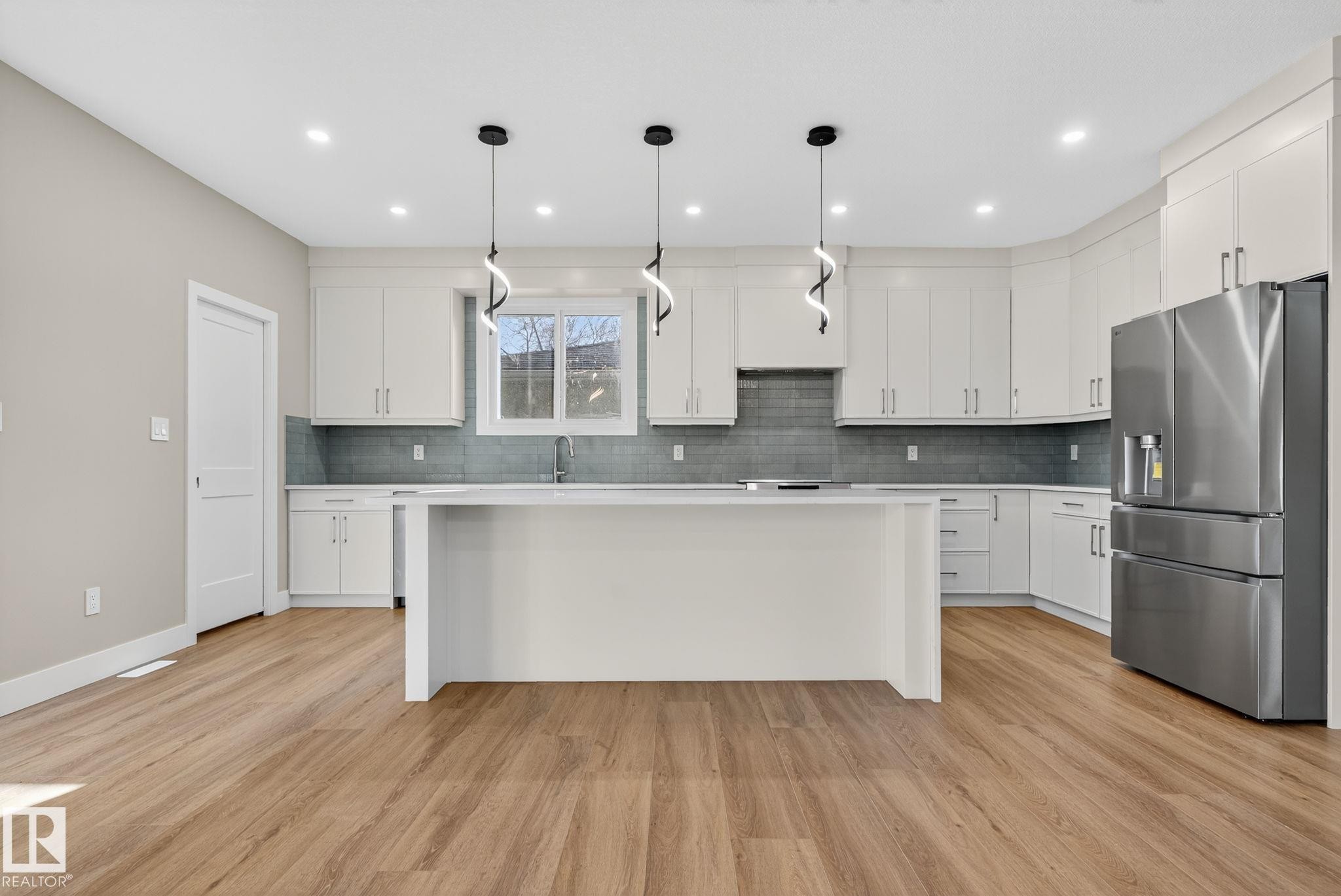 Kitchen featuring white cabinetry, a central island, stainless steel appliances, wood-finish flooring, and pendant lighting - 9736 73 Avenue Nw, Edmonton, AB