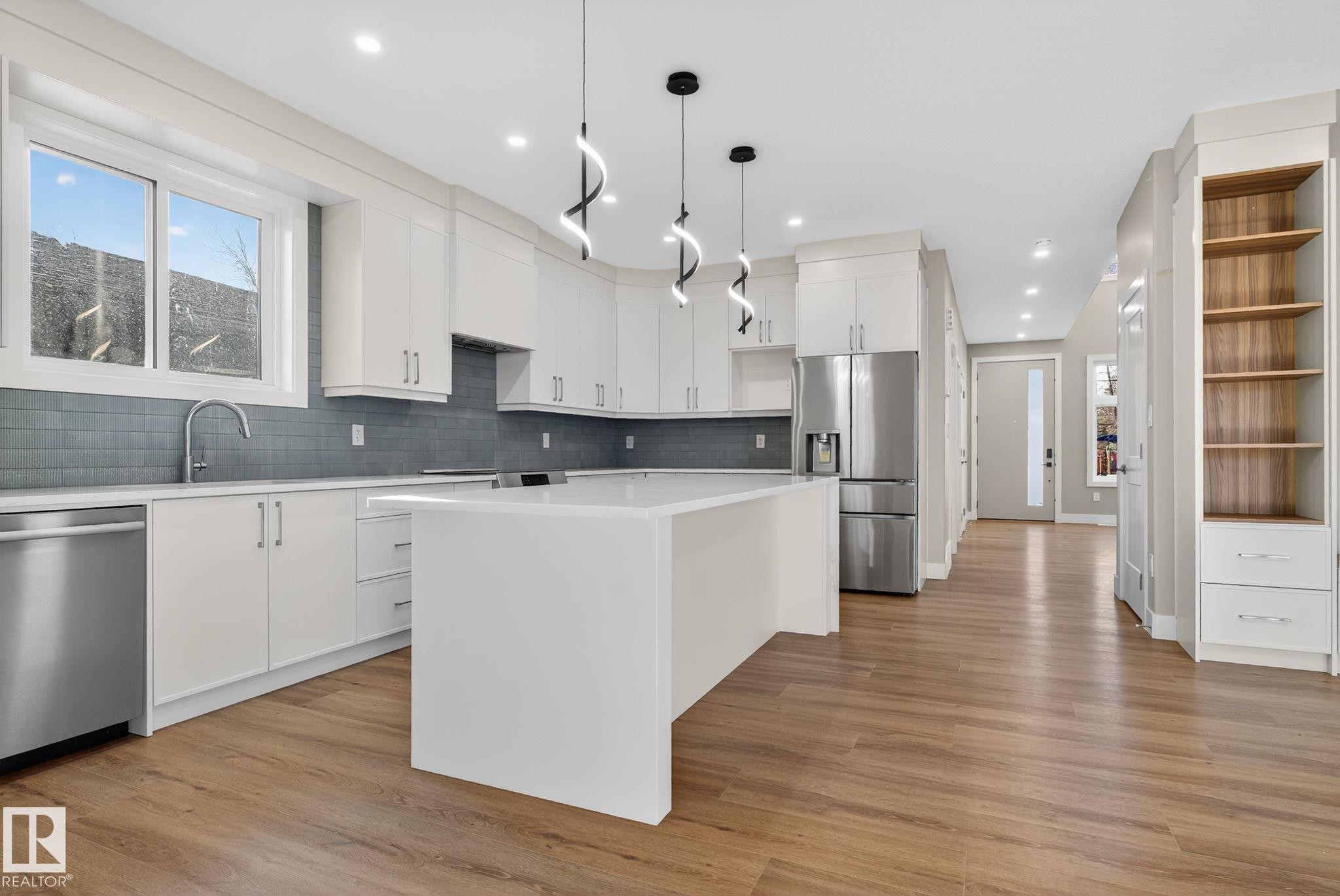 Modern kitchen featuring white cabinetry, stainless steel appliances, a center island with a solid surface countertop, and wood-finish flooring - 9736 73 Avenue Nw, Edmonton, AB
