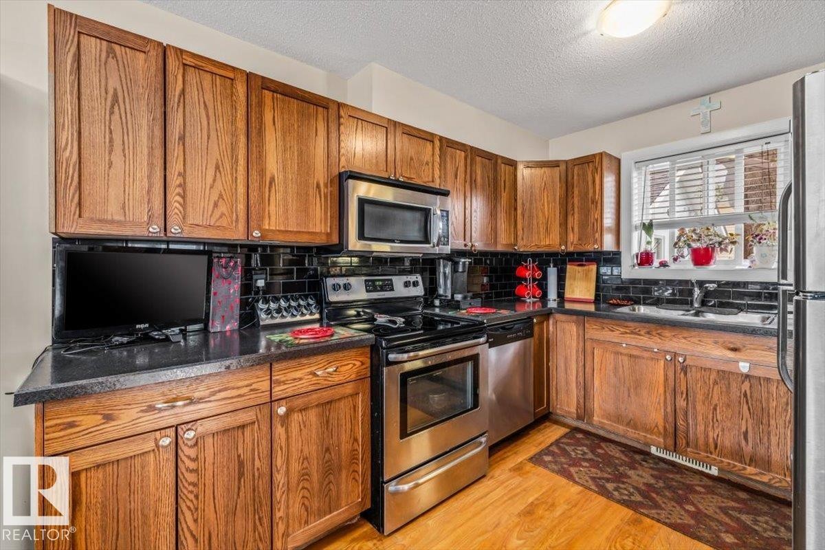 Wood-finish cabinetry complemented by dark countertops, a subway tile backsplash, and stainless steel appliances - 11436 88 Street Nw, Edmonton, AB - Indoor Photo Showing Kitchen
