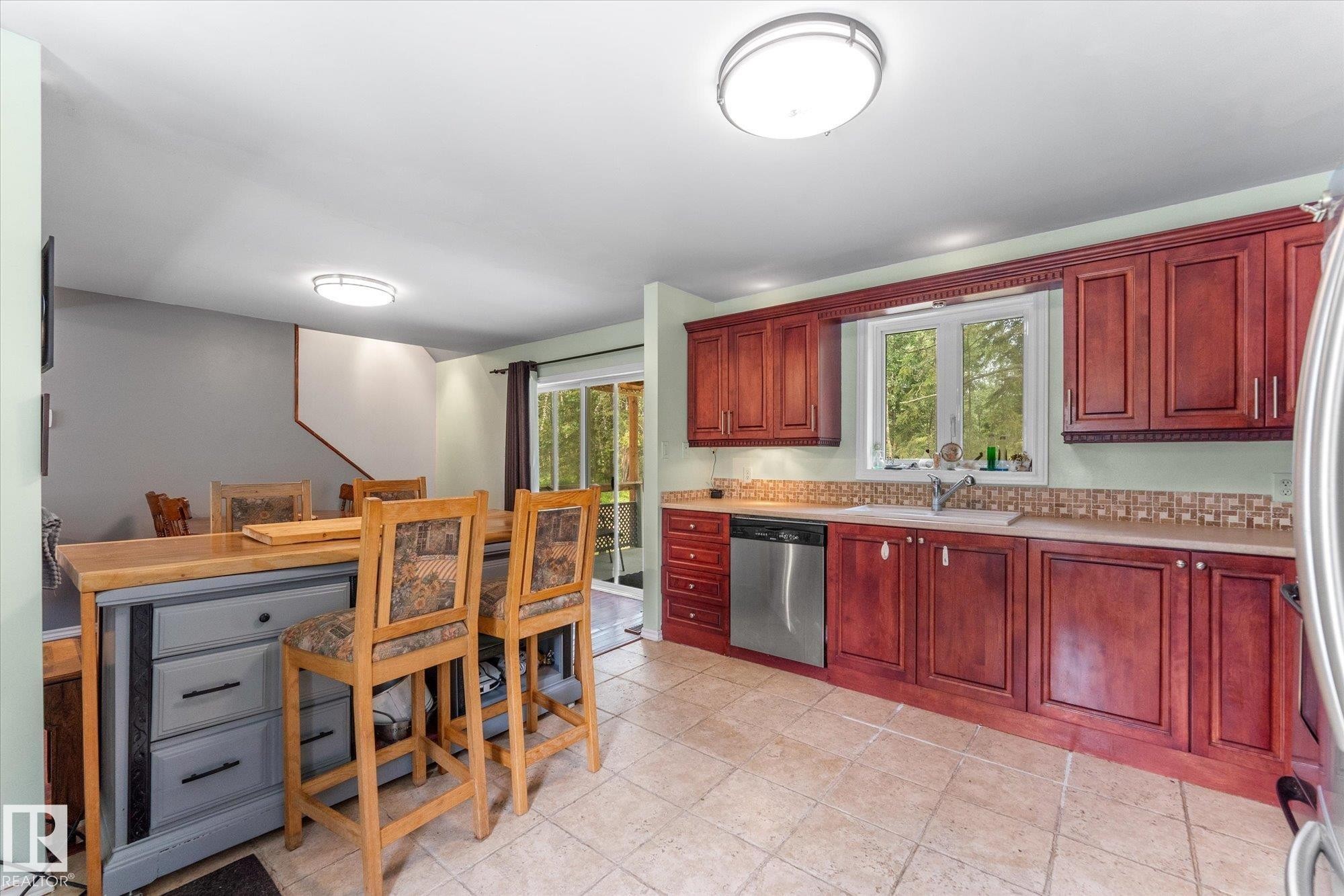 Kitchen featuring cherry wood-finish cabinetry, stainless steel dishwasher, tile flooring, window with natural light, and an integrated breakfast bar - 2, 59031 Range Rd 232, Rural Thorhild County, AB - Indoor
