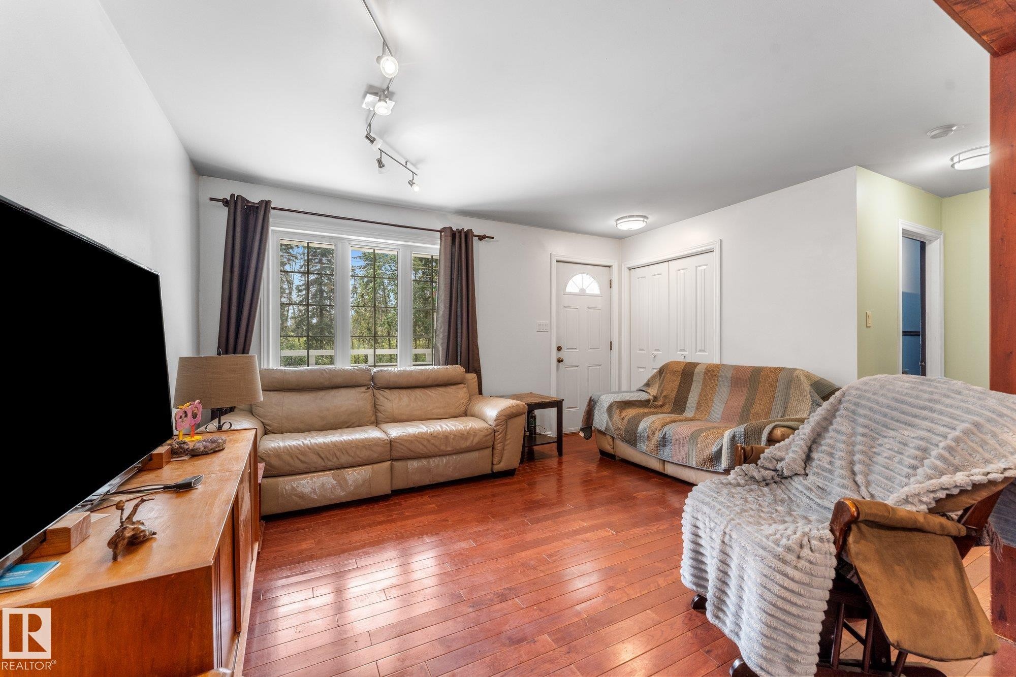 Bright living area featuring wood-finish flooring, a window offering natural light, and a prominent entry door - 2, 59031 Range Rd 232, Rural Thorhild County, AB - Indoor Photo Showing Living Room