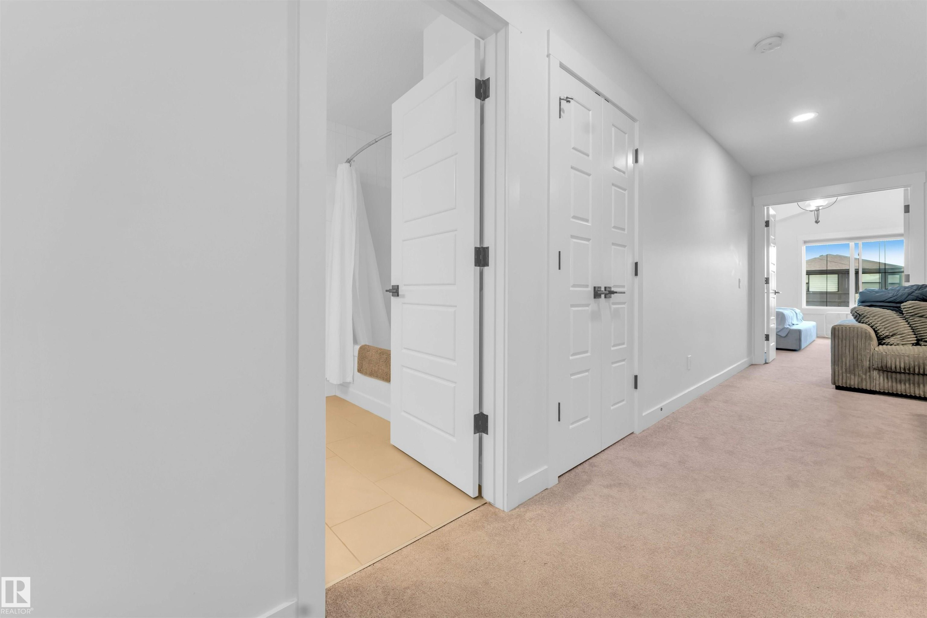 Carpeted hallway with white interior doors, recessed lighting, and a tiled bathroom floor - 3236 Chernowski Way Sw, Edmonton, AB - Indoor
