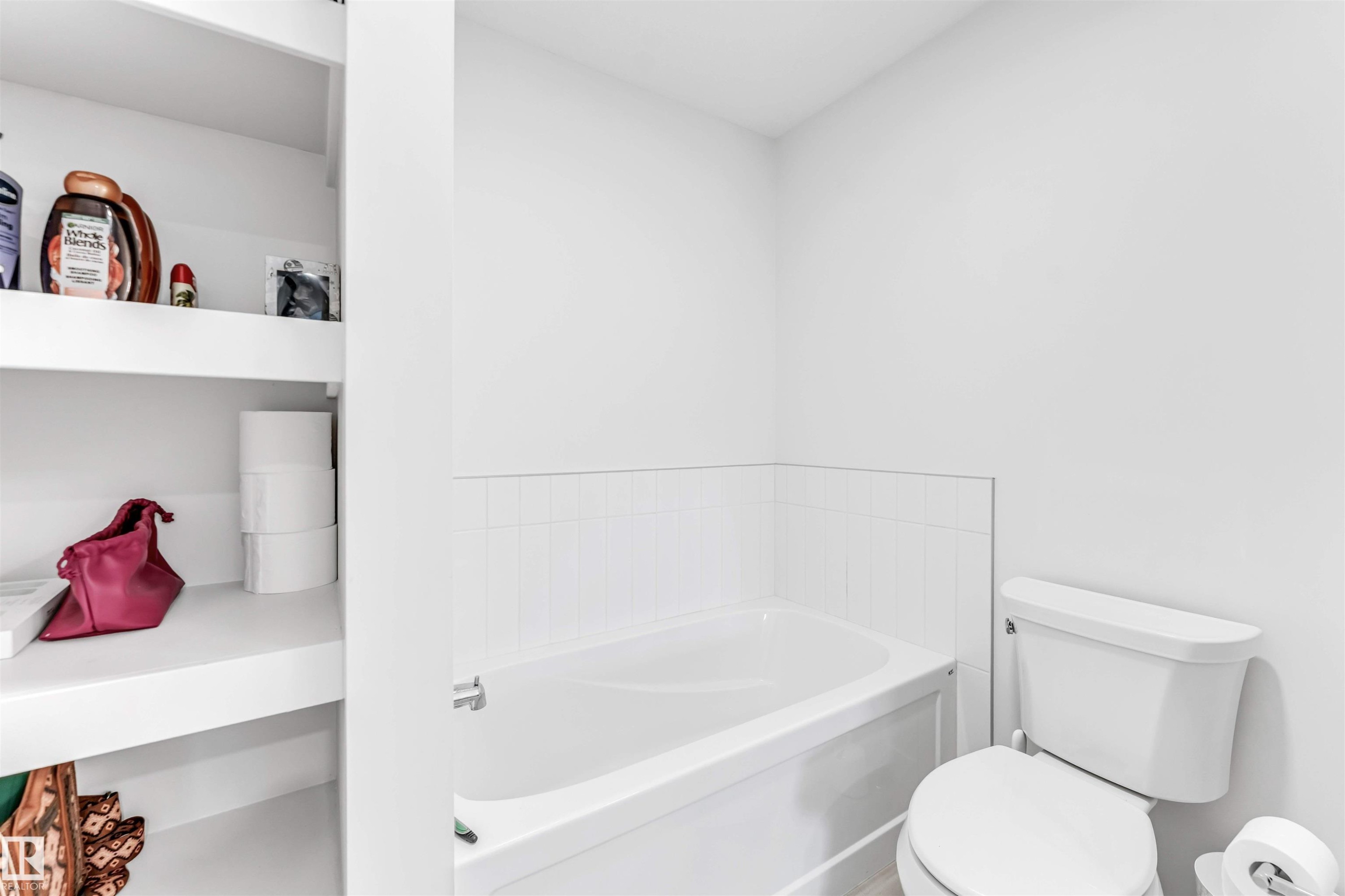 Built-in shelving, white ceramic toilet, white drop-in bathtub, and ceramic tile wainscoting - 3236 Chernowski Way Sw, Edmonton, AB - Indoor Photo Showing Bathroom