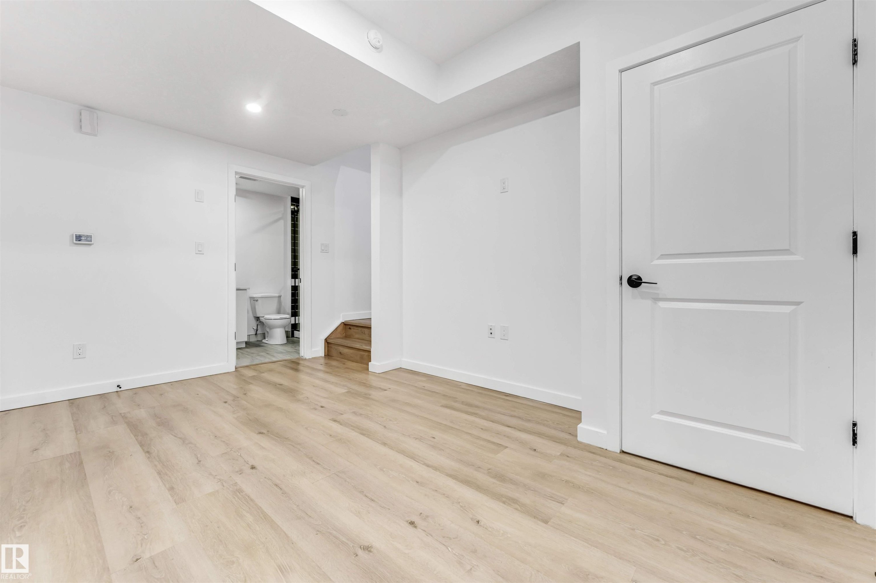 Basement: Light wood-finish flooring, recessed lighting, white walls, and a white two-panel interior door with a matte black knob - 3236 Chernowski Way Sw, Edmonton, AB - Indoor Photo Showing Other Room