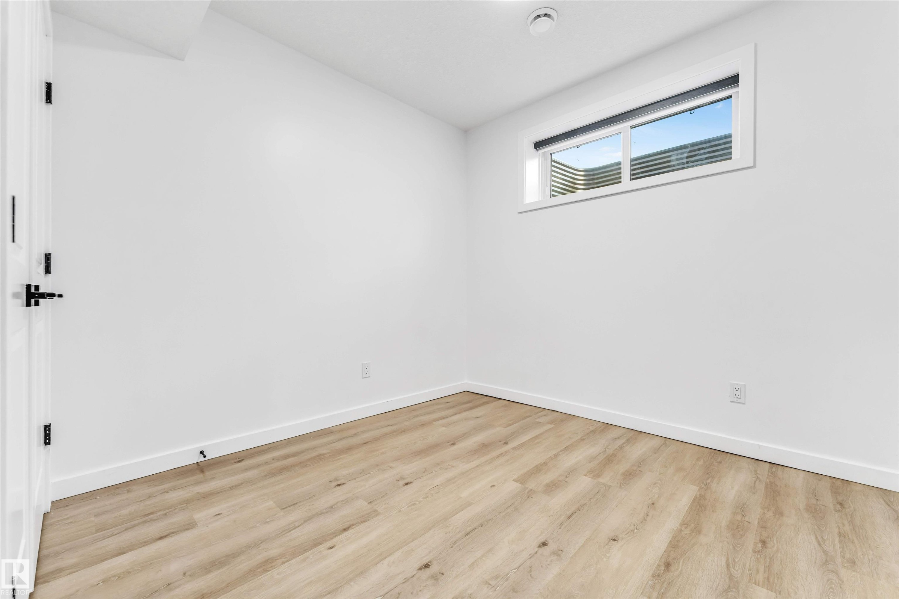 Recessed window with exterior enclosure, wood-finish flooring, white walls, and a white paneled door with black hardware - 3236 Chernowski Way Sw, Edmonton, AB - Indoor Photo Showing Other Room