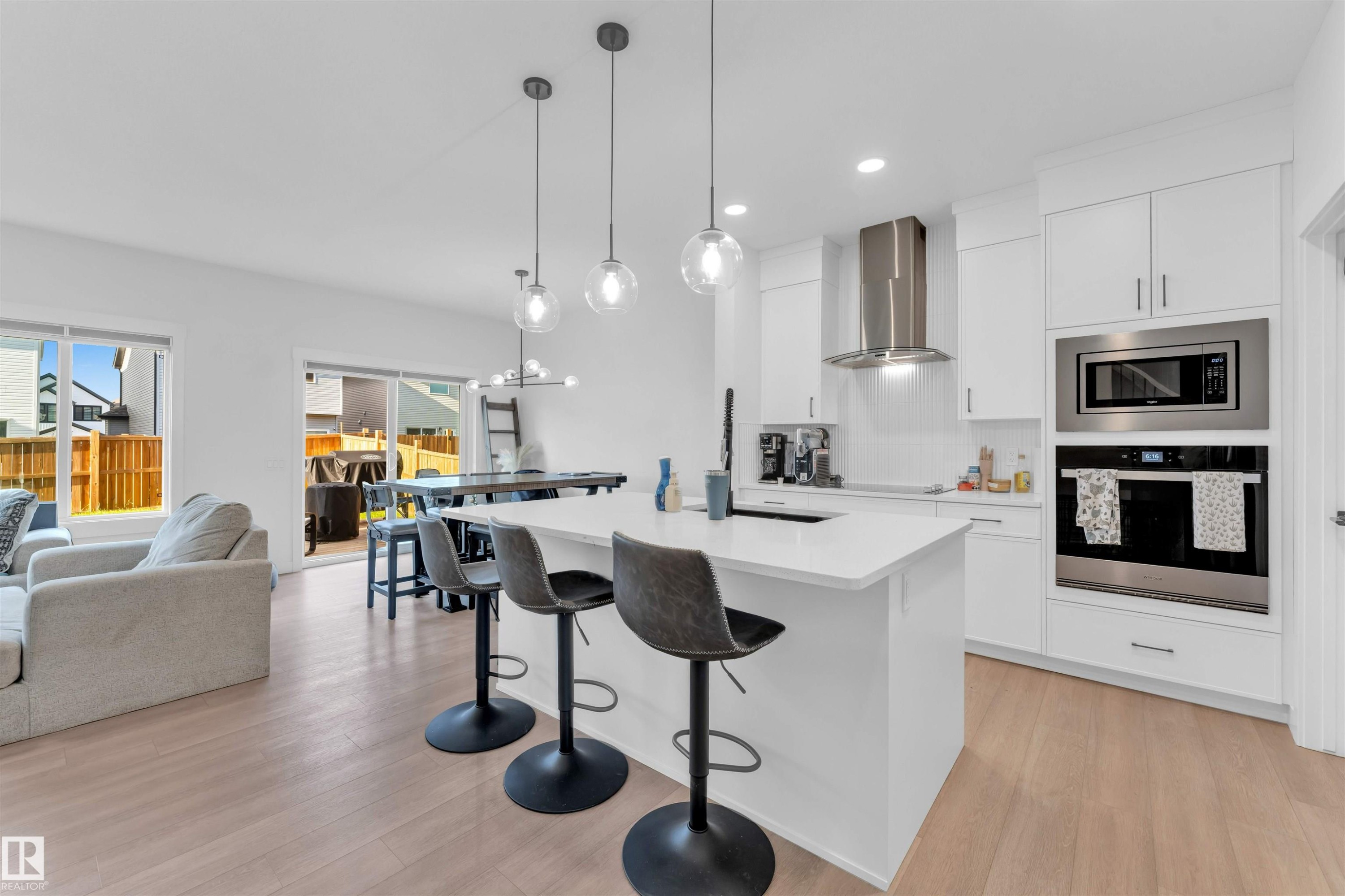 Open-concept living area with wood-finish flooring, white cabinetry, integrated stainless steel appliances, and a kitchen island with pendant lighting - 3236 Chernowski Way Sw, Edmonton, AB - Indoor Photo Showing Kitchen With Upgraded Kitchen
