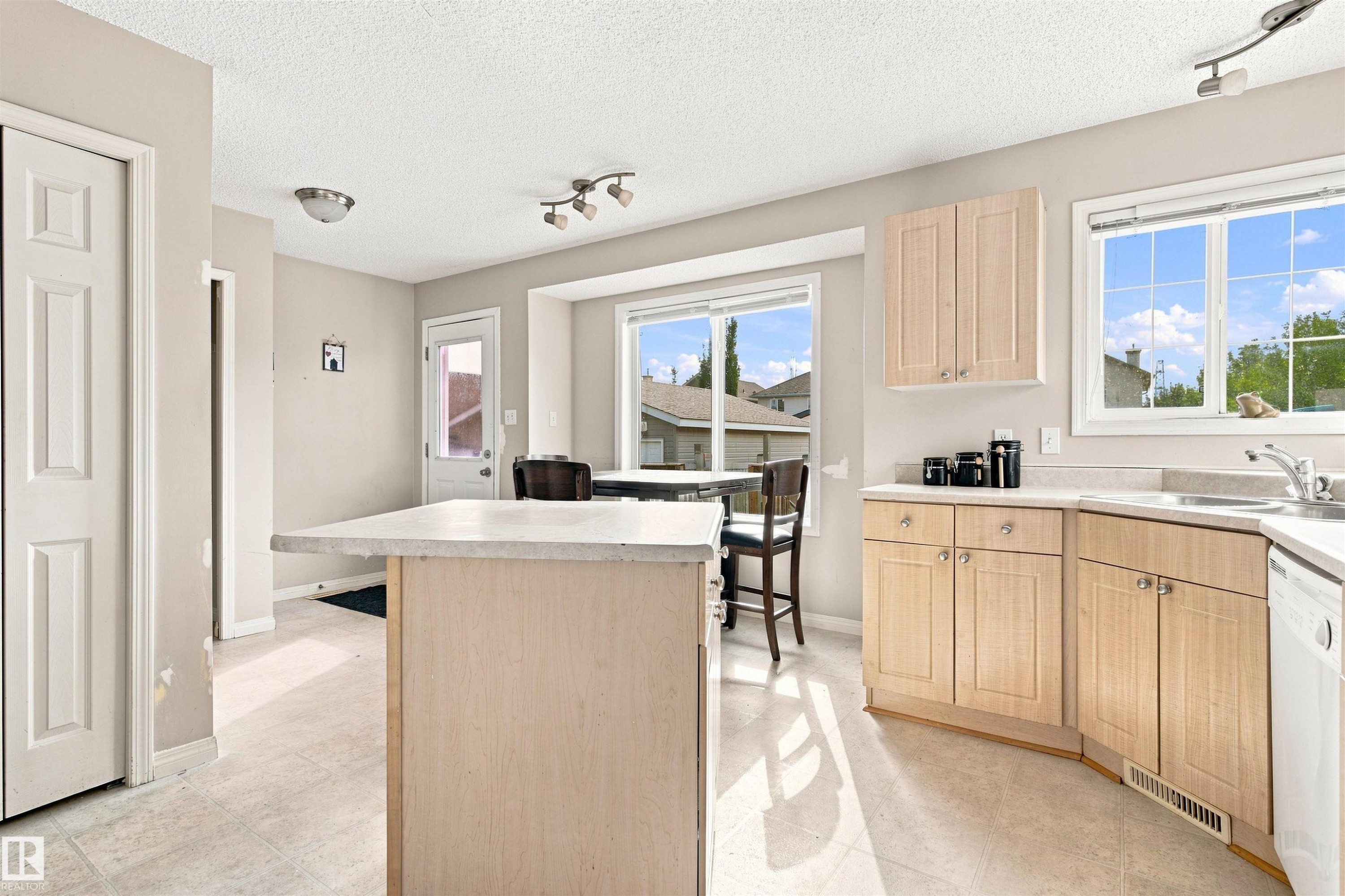 Kitchen island with light-toned cabinetry, light-colored countertops, and tile flooring - 204 84 Street Sw, Edmonton, AB - Indoor Photo Showing Kitchen With Double Sink