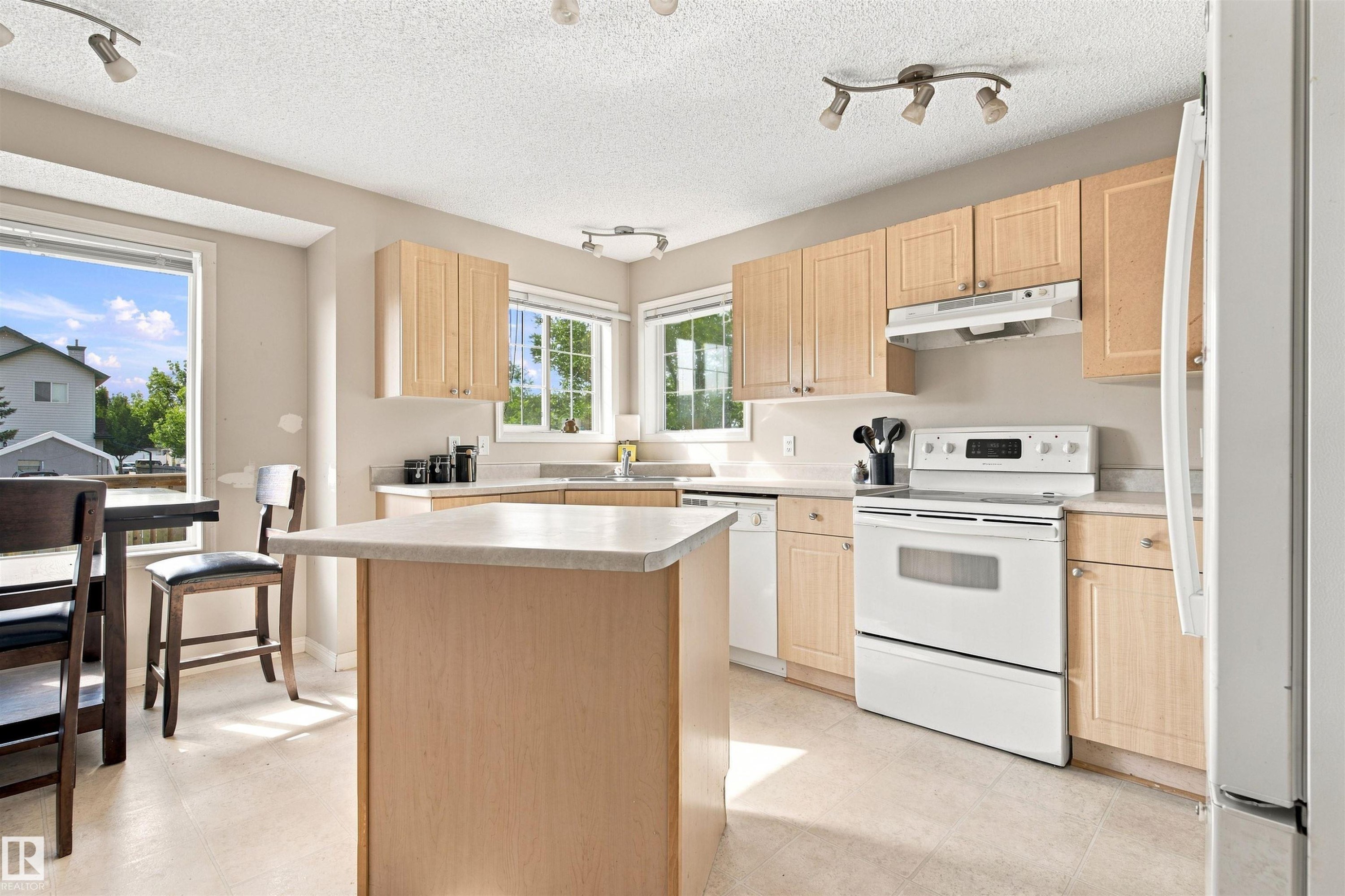 Light wood-finish cabinetry, solid surface countertops, white appliances, recessed lighting, and a center island - 204 84 Street Sw, Edmonton, AB - Indoor Photo Showing Kitchen With Double Sink